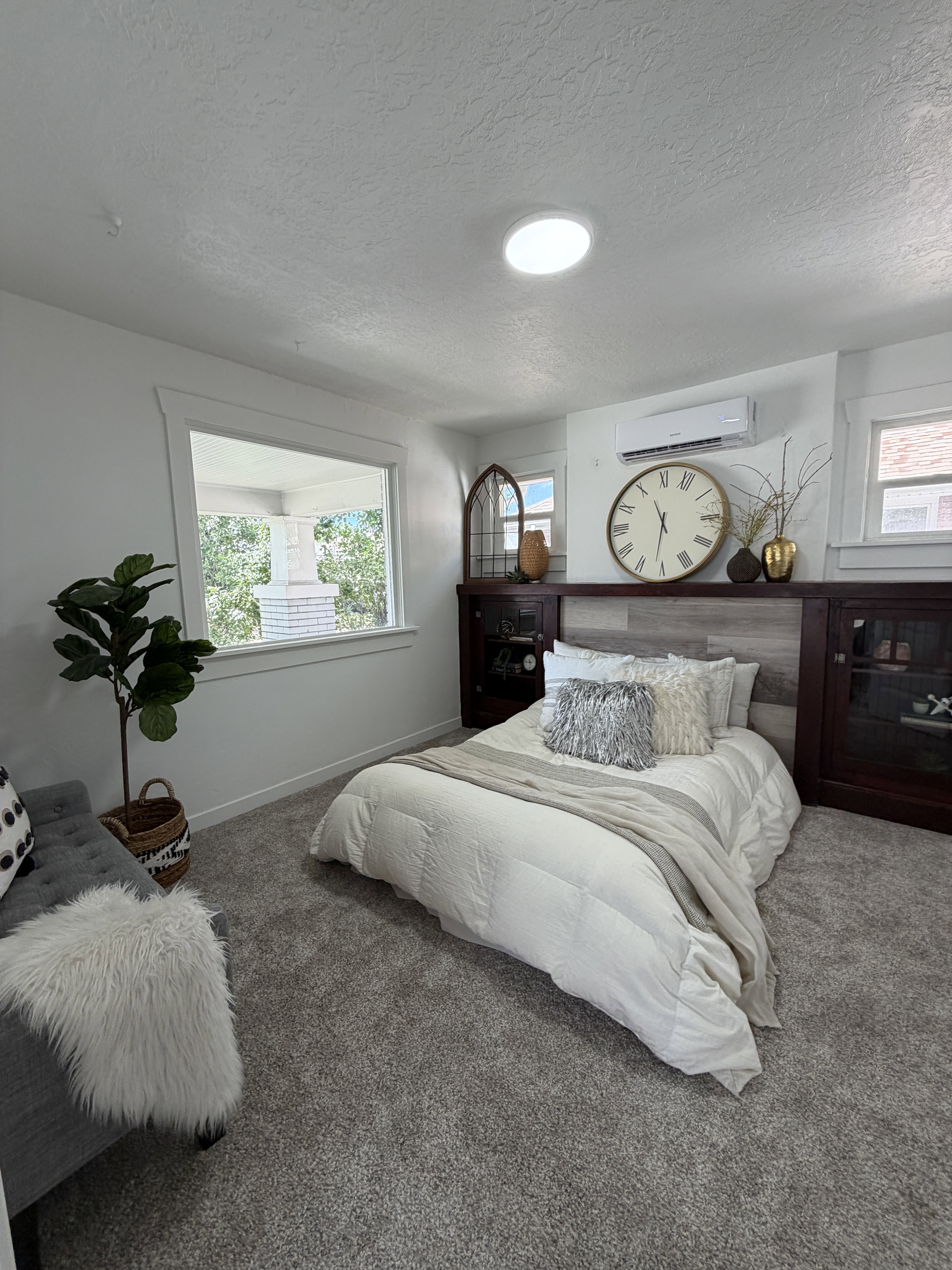 Recessed ceiling lighting, plush gray carpeting, built-in dark wood cabinetry with glass fronts, wood-finish accent wall, and a ductless mini-split system