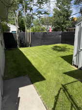 Expansive backyard featuring a green lawn, mature trees, concrete patio, and dark privacy fencing