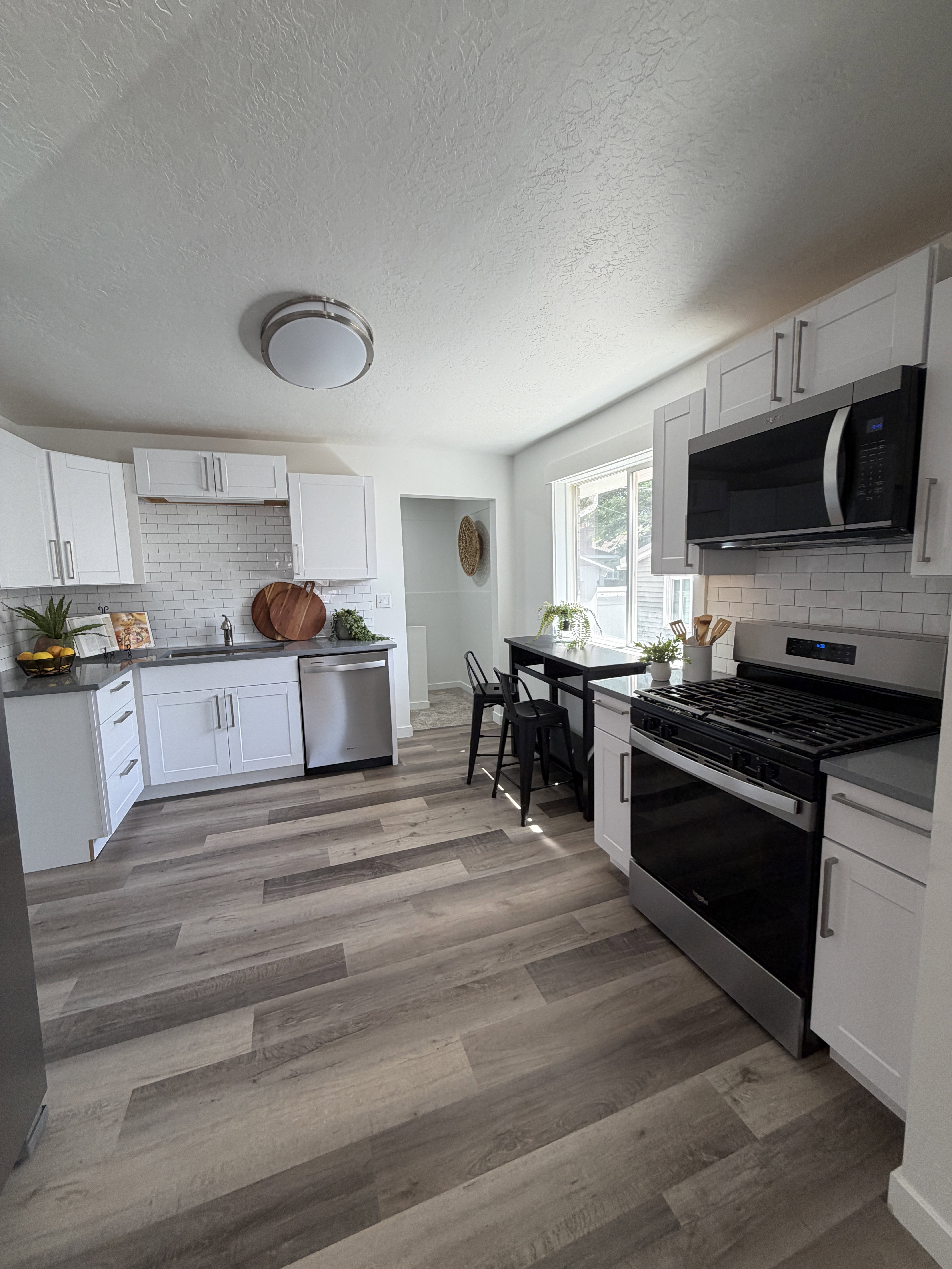 Kitchen featuring wood-finish plank flooring, white shaker cabinetry, stainless steel appliances, dark countertops, and a white subway tile backsplash