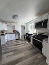 Kitchen featuring wood-finish plank flooring, white shaker cabinetry, stainless steel appliances, dark countertops, and a white subway tile backsplash
