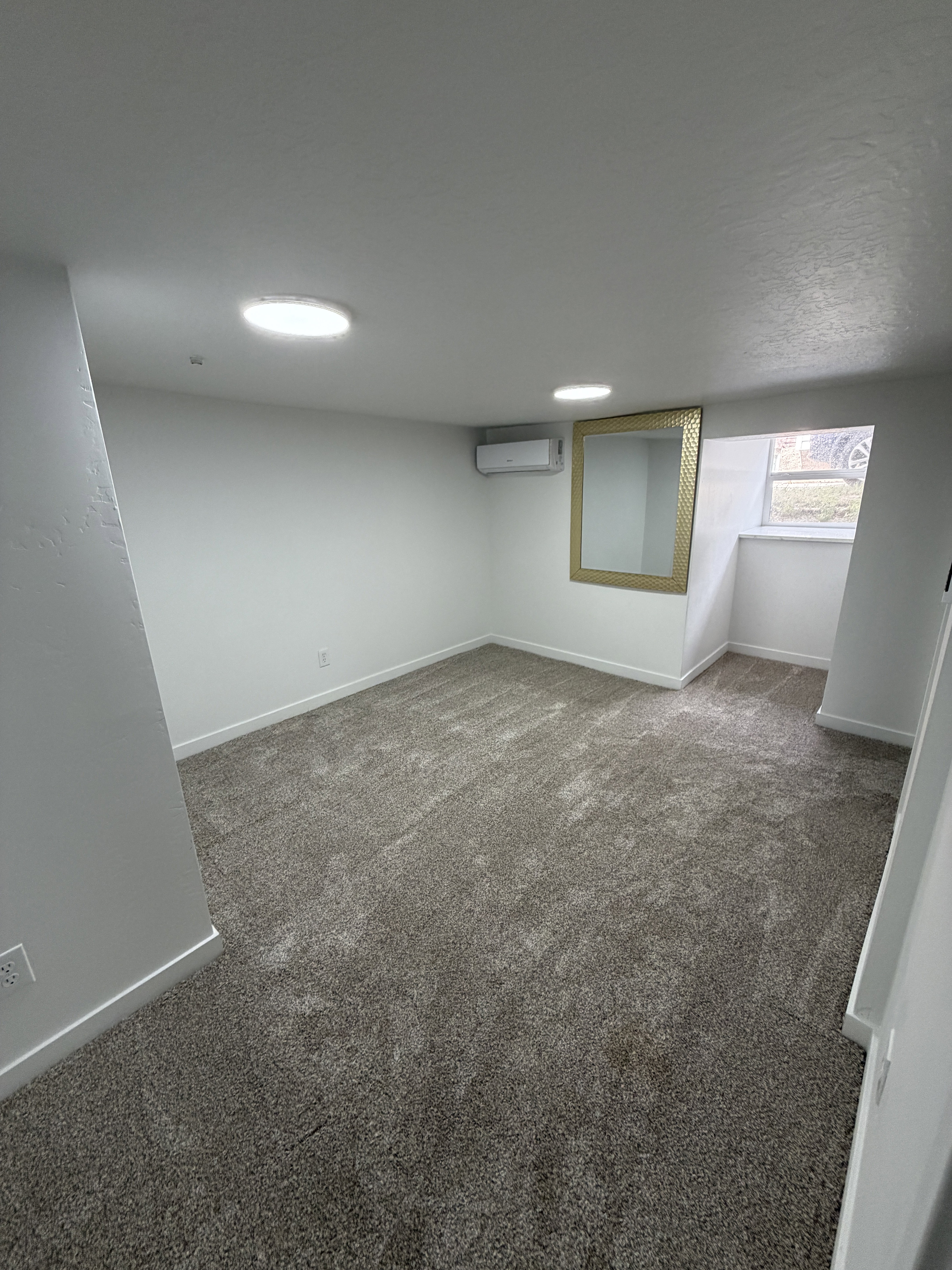Carpeted room featuring recessed lighting, a wall-mounted mini-split unit, and a window with a deep sill