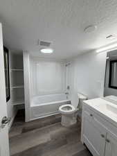 Bathroom featuring wood-finish flooring, a white vanity with a single basin sink, a white bathtub with a shower surround, and integrated shelving