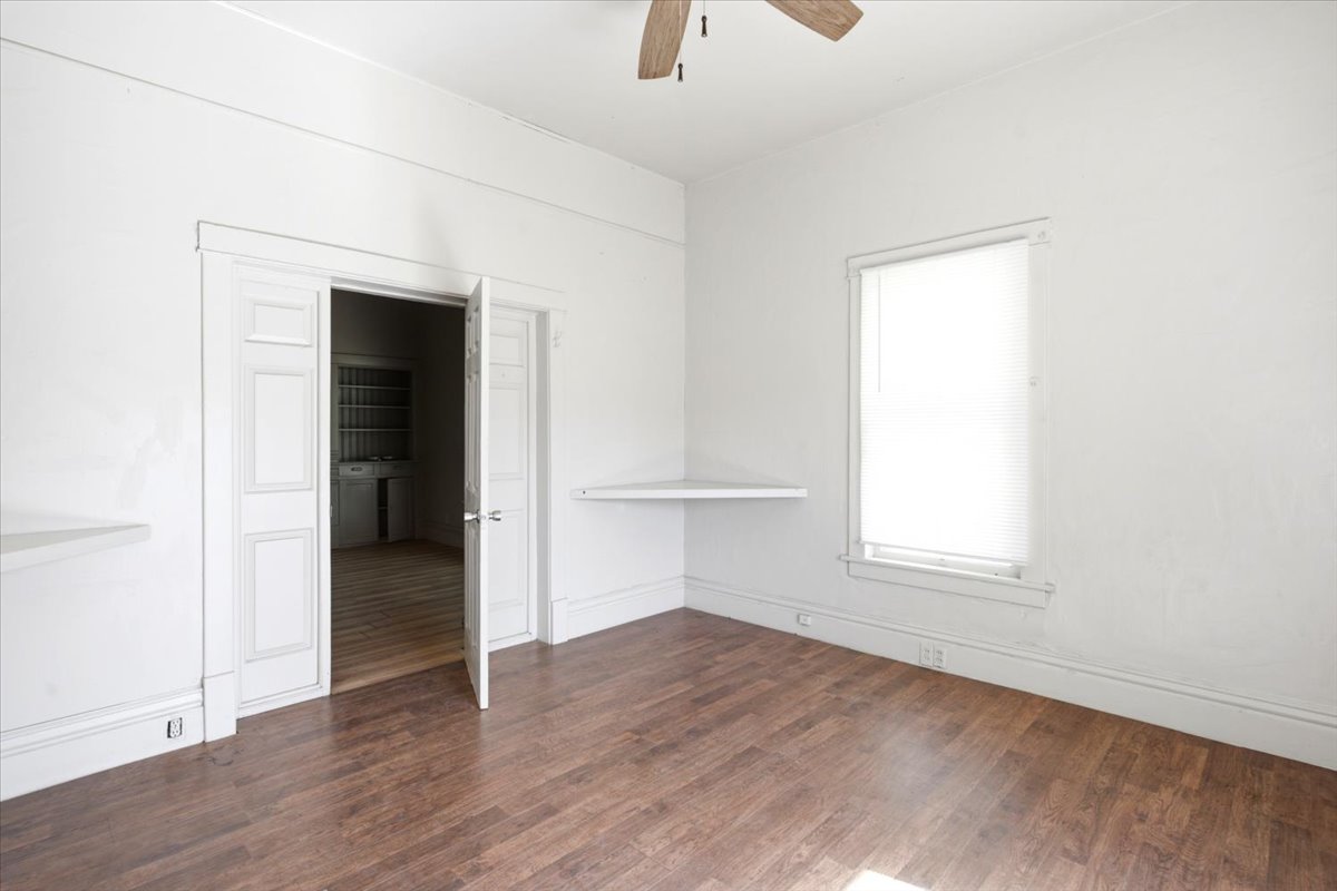 Room featuring wood-finish flooring, a ceiling fan, and a built-in corner shelf
