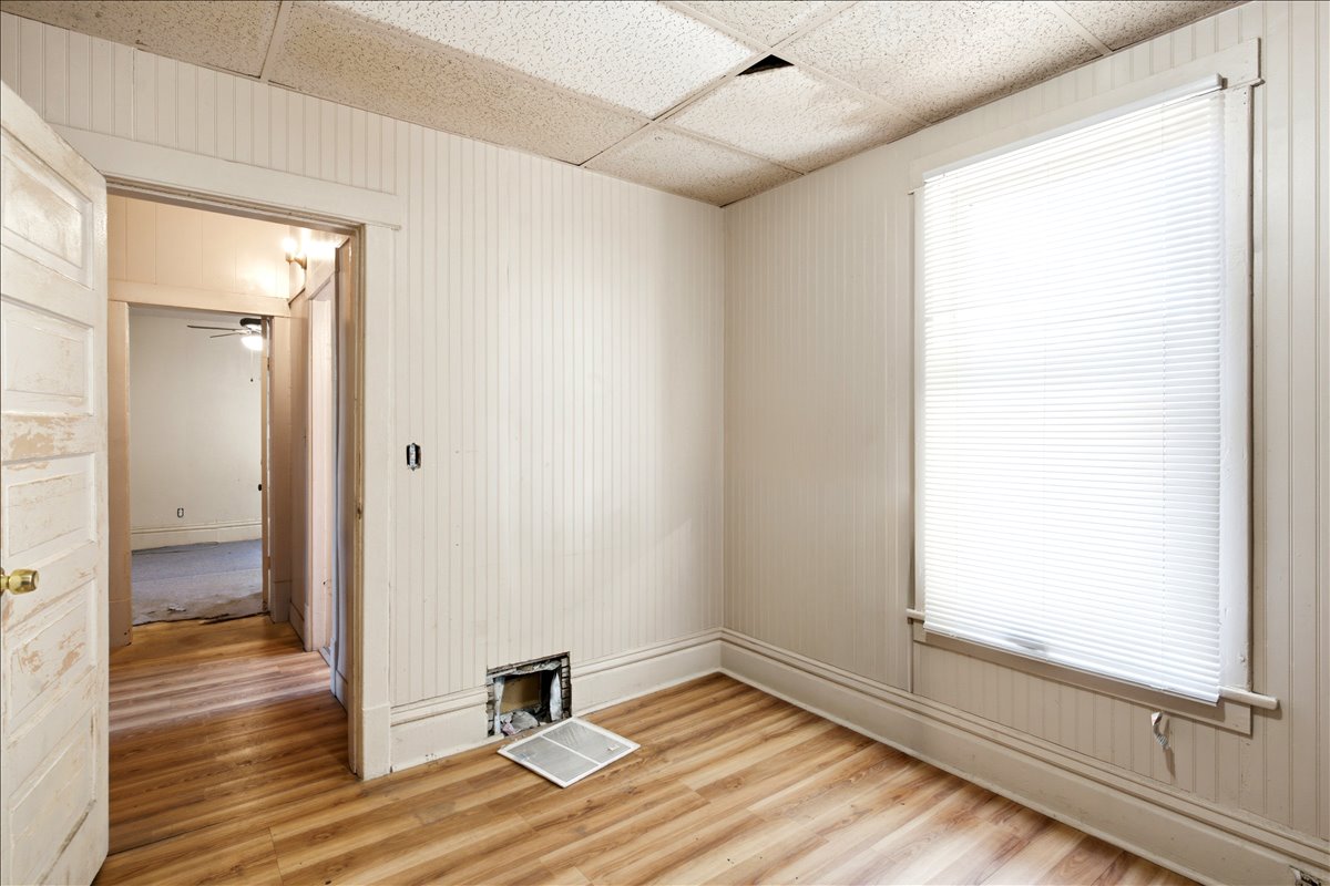 Room featuring wood-finish flooring, vertical paneling on walls, and a window with blinds