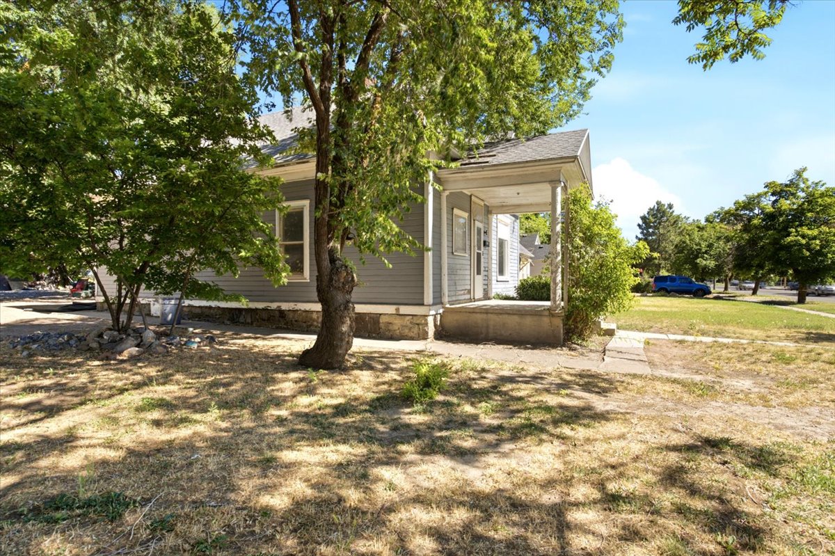 Gray siding exterior featuring a covered porch with white columns, a pitched roof, and mature trees providing natural shade