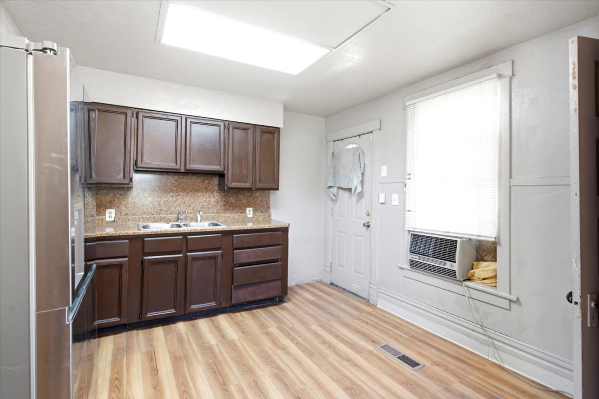 Kitchen featuring wood-finish flooring, dark wood cabinetry, and a light-toned countertop with a matching backsplash