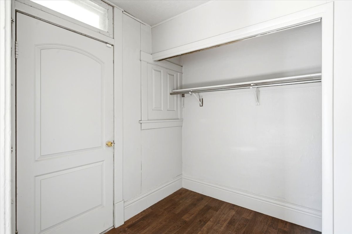 Bedroom featuring wood-finish flooring, white walls, and a built-in closet with hanging rods