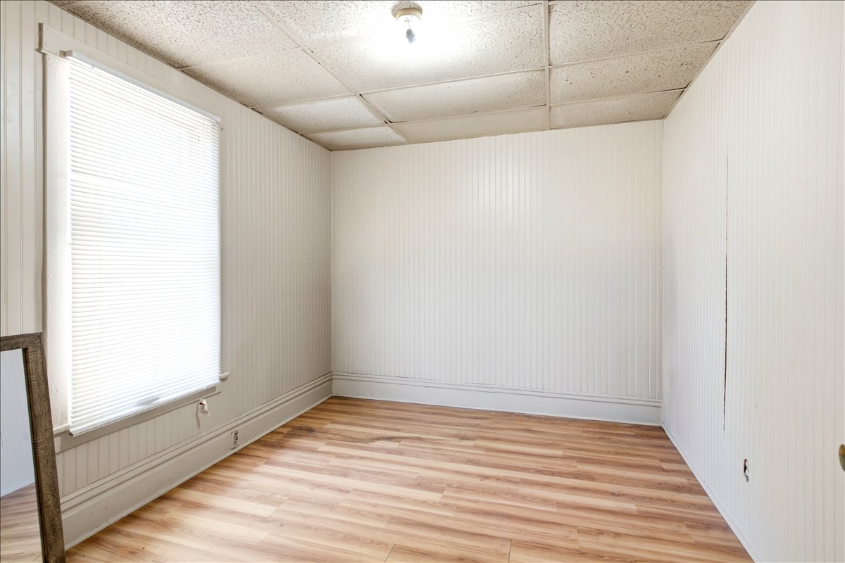 Room featuring wood-finish flooring, vertical paneling on walls, and a window with blinds