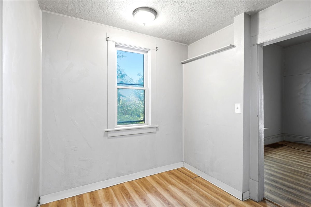Room featuring light wood-finish flooring, a double-hung window with white trim, and a flush-mount ceiling light fixture