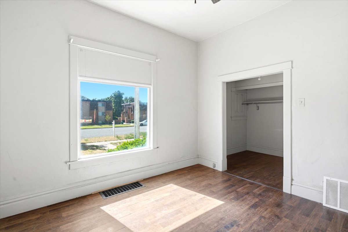 Bright room featuring wood-finish flooring, a large window with roller shades, and a built-in closet with shelving and a hanging rod