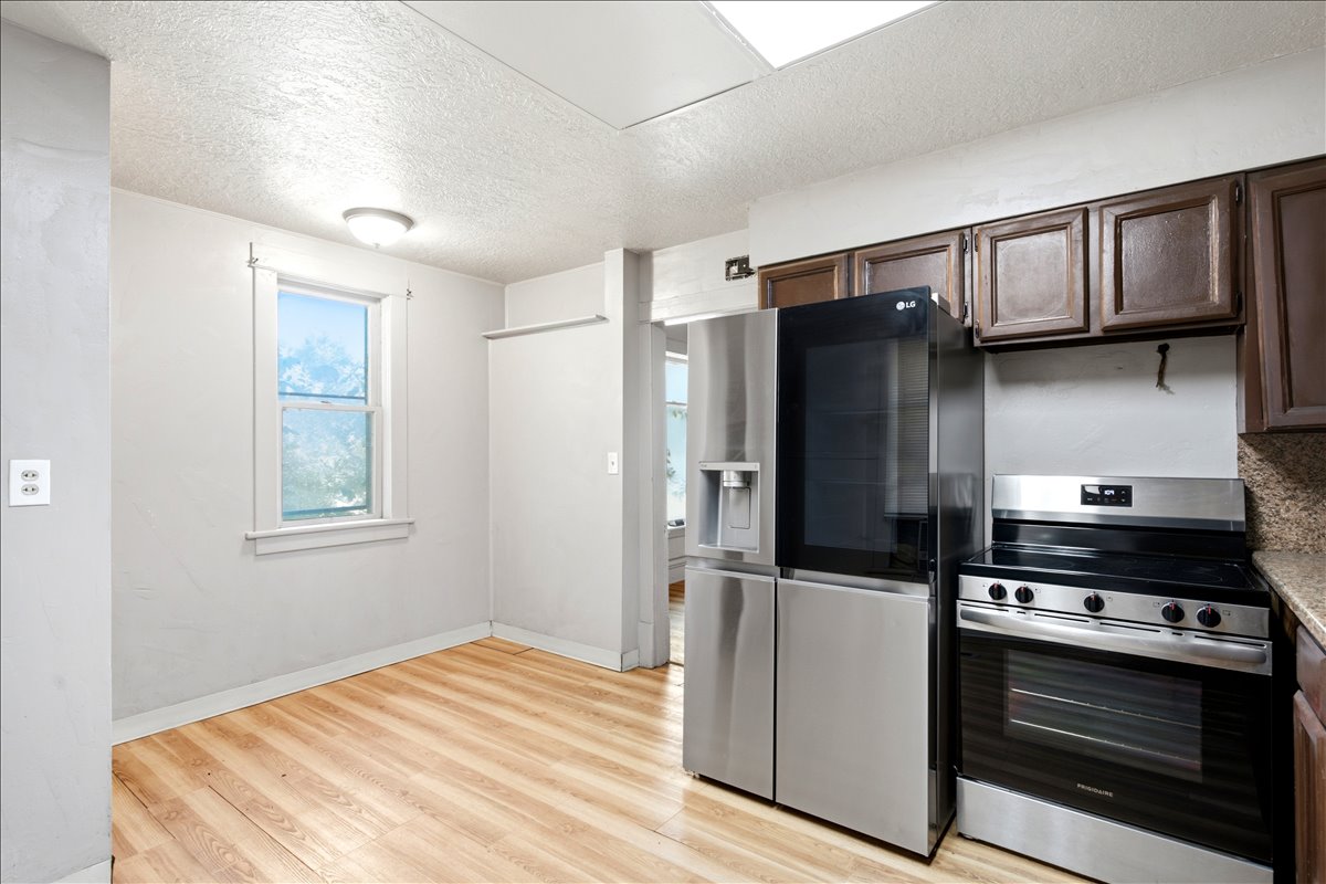 Kitchen area featuring wood-finish flooring, a window providing natural light, a stainless steel refrigerator, and a stainless steel range oven