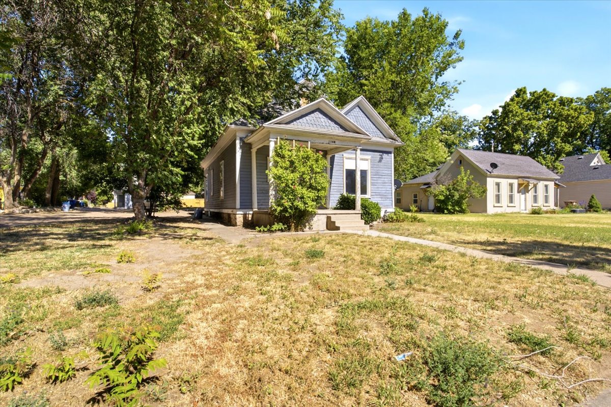 Single-story property featuring light blue siding with white trim, a covered front porch, and mature trees providing shade