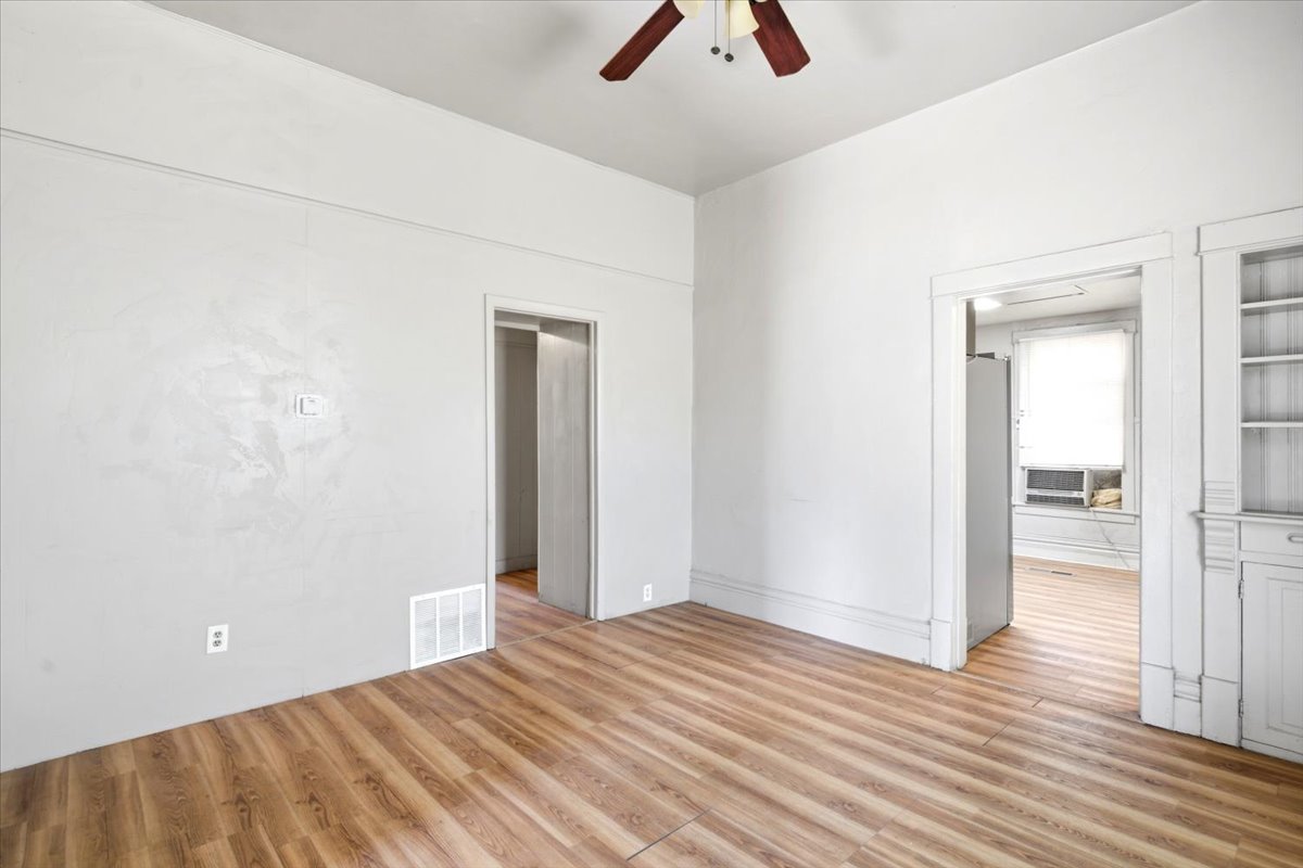 Spacious interior room featuring wood-finish flooring, light-toned walls, a ceiling fan, and built-in shelving