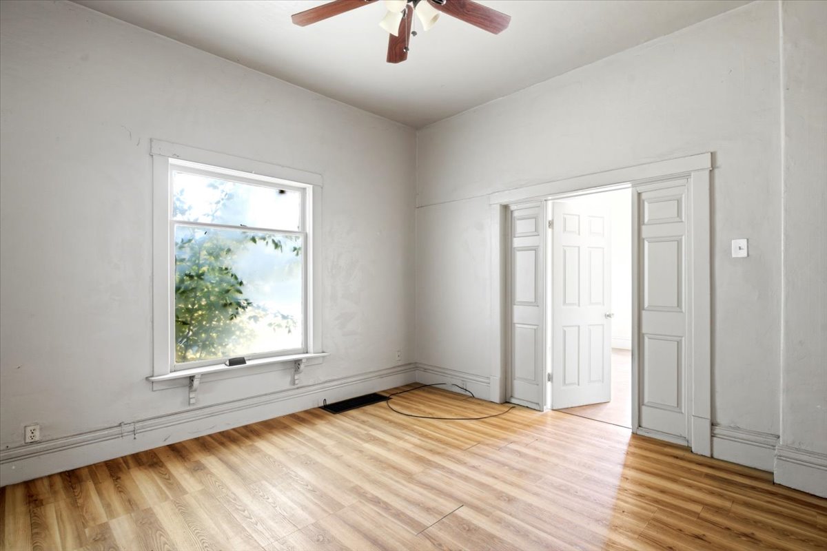 Bright room featuring wood-finish flooring, a ceiling fan with light kit, and a large window with white trim