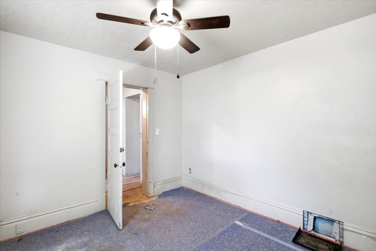Room featuring a ceiling fan with light fixture, white walls, and a door frame