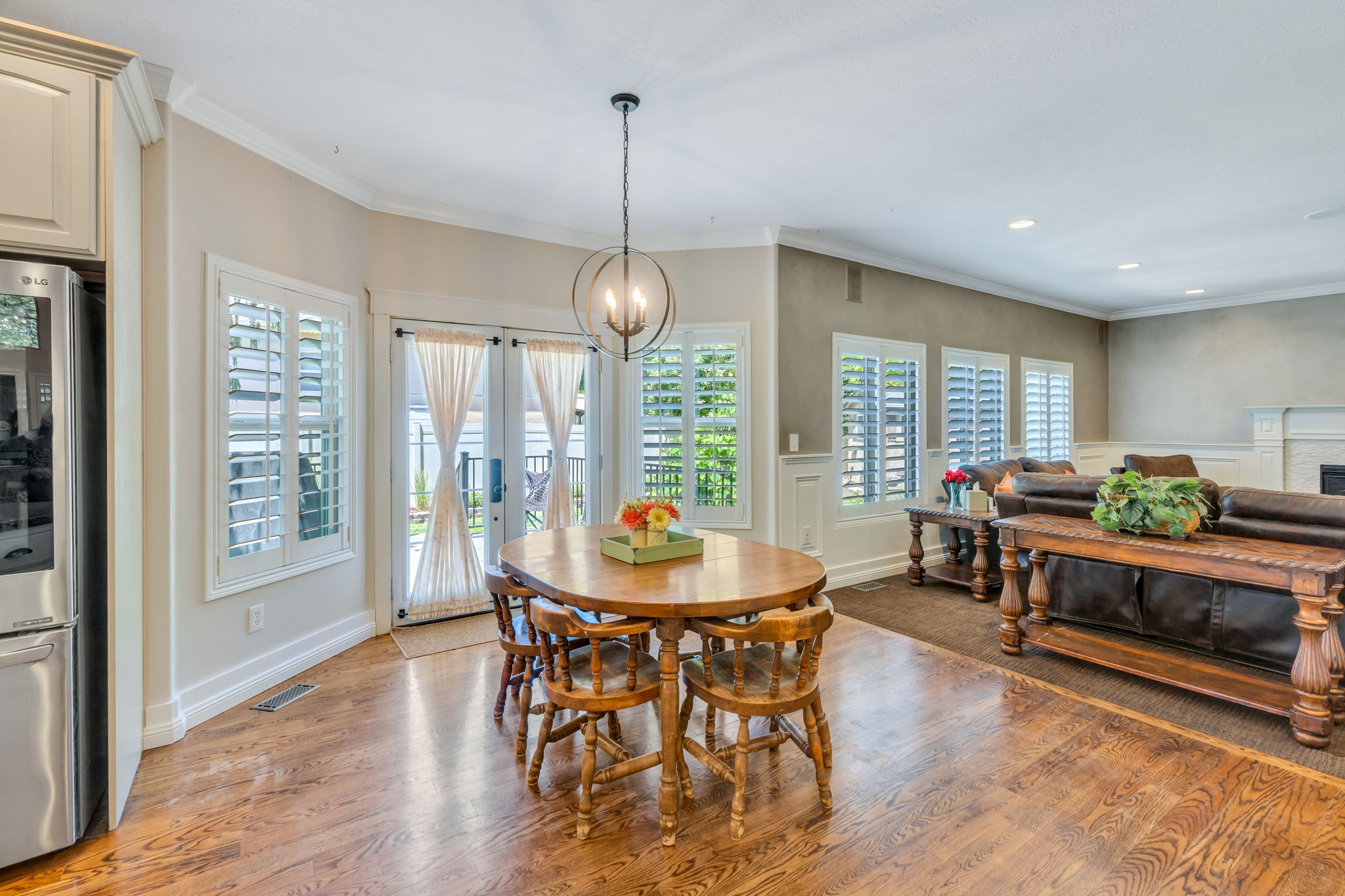 Open-concept living space featuring wood-finish flooring, white plantation shutters, crown molding, and a modern spherical chandelier