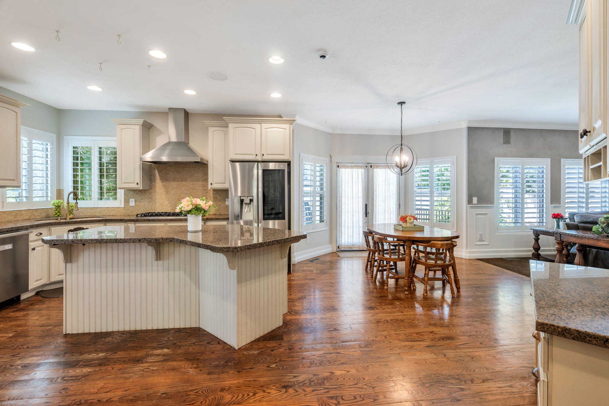 Kitchen featuring a large island with a granite countertop, stainless steel appliances, wood-finish flooring, white plantation shutters, and a spherical chandelier