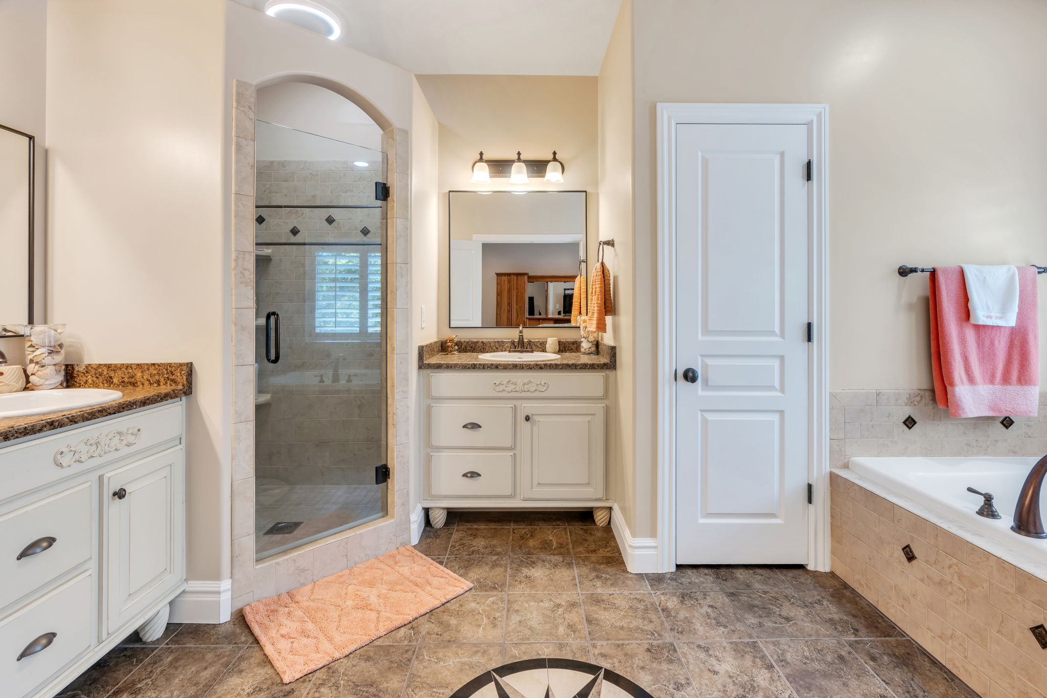 Bathroom featuring a glass-enclosed shower with an arched entry, a built-in soaking tub with a tiled surround, two vanity sinks with patterned countertops, and patterned tile flooring