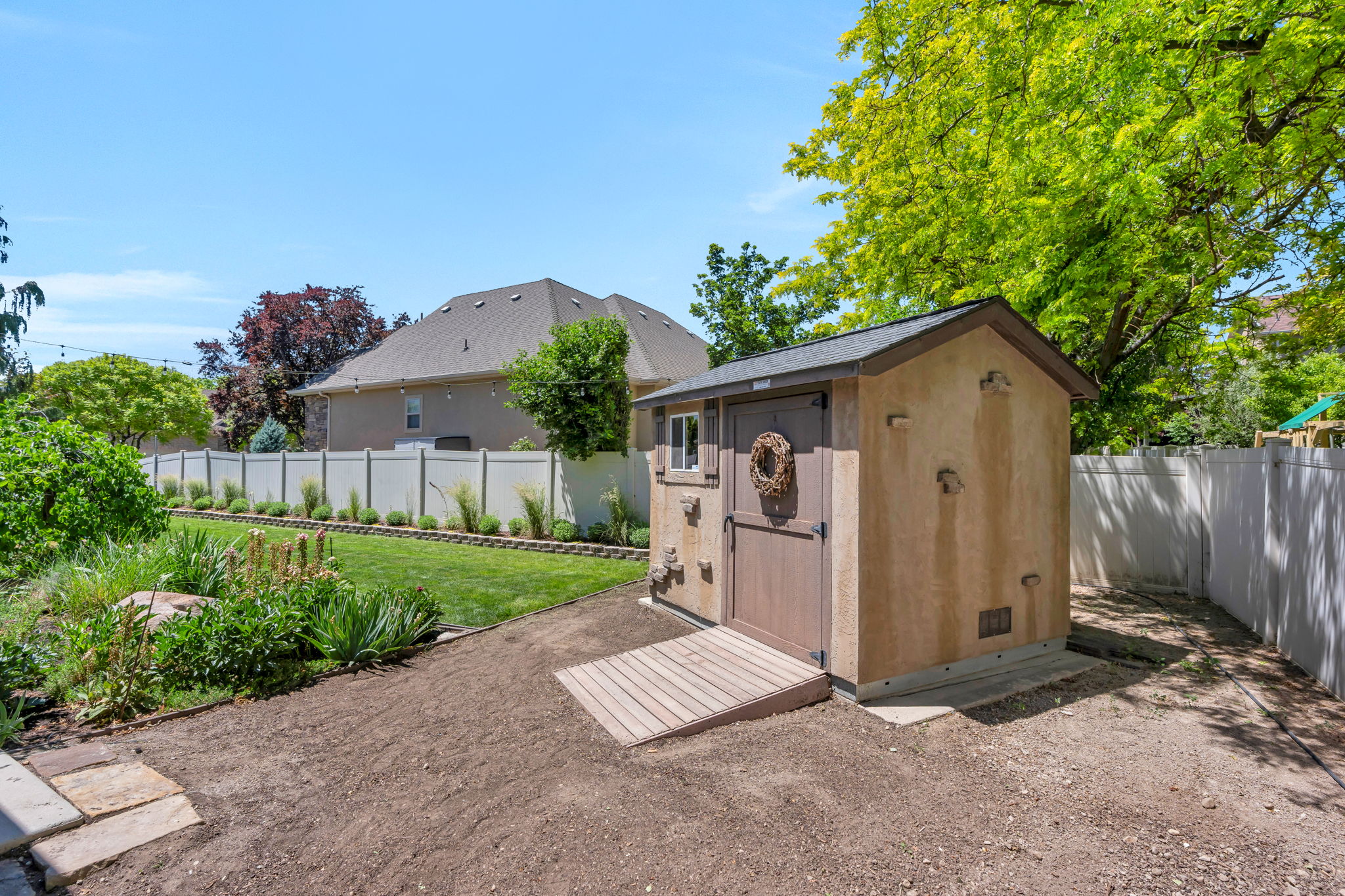 Backyard featuring a stucco-finish shed with a shingled roof, a wooden ramp, and a vinyl privacy fence