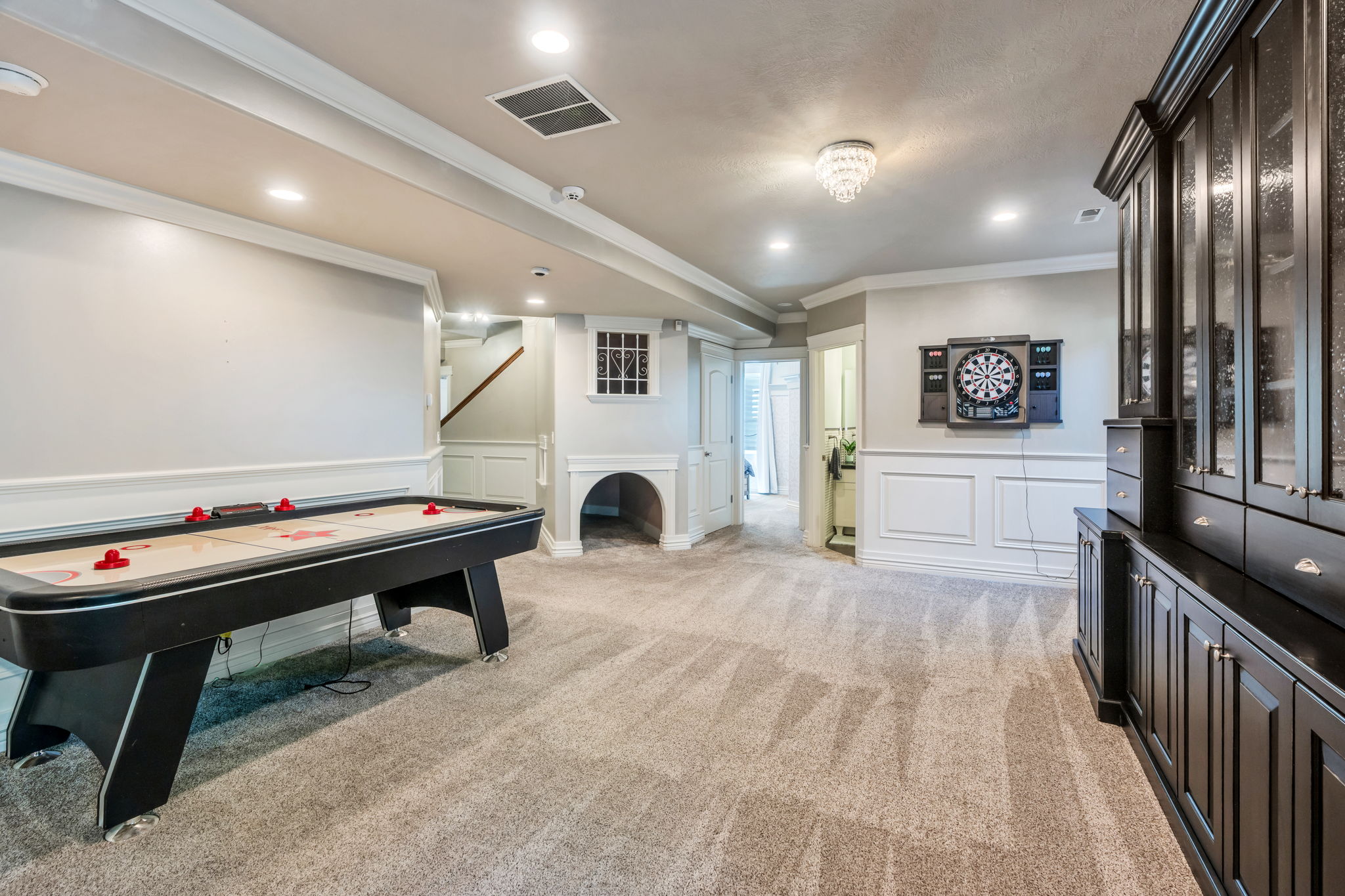 Spacious entertainment area featuring wall paneling, recessed lighting, and a built-in dark wood cabinetry unit with glass-front display cabinets