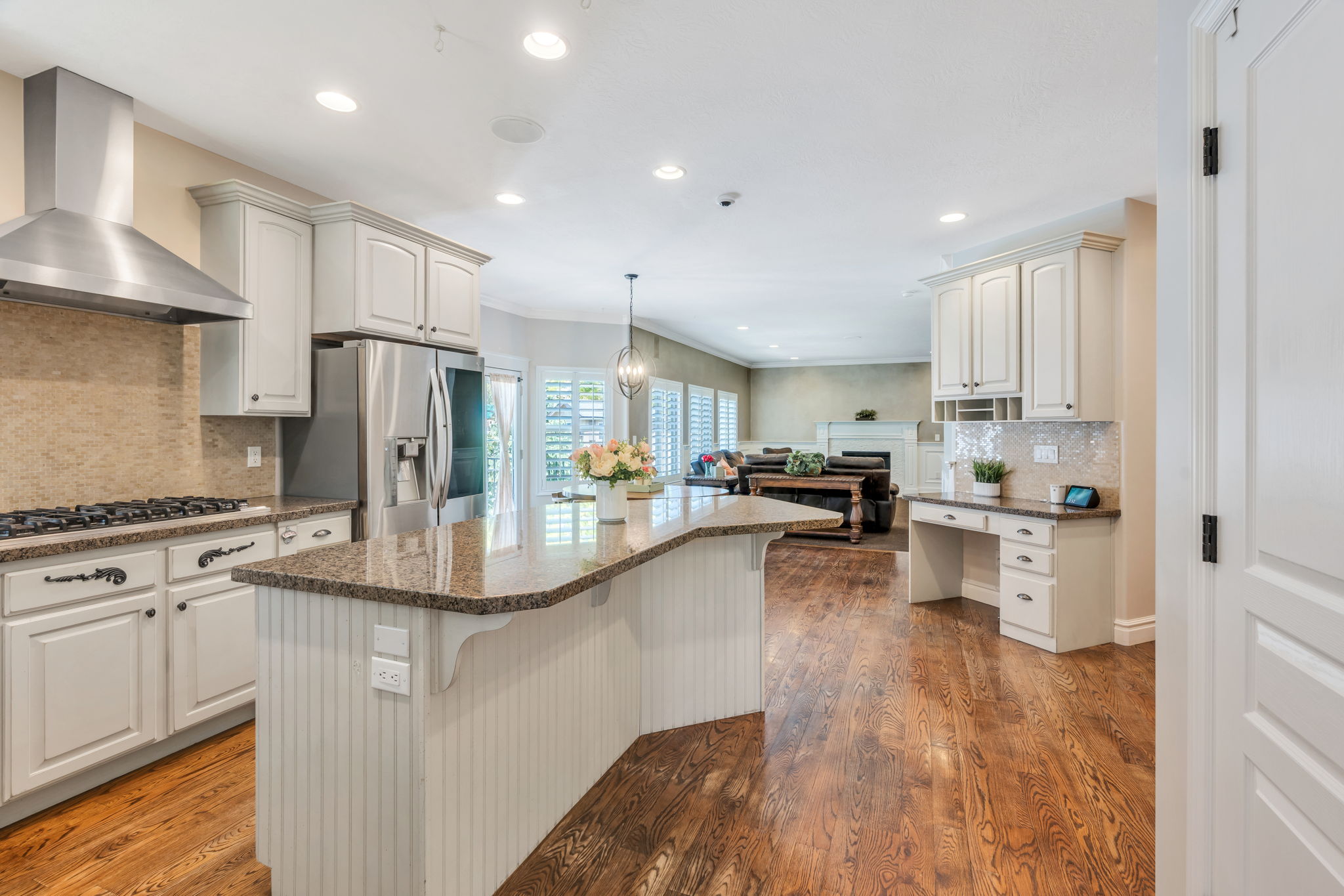 Expansive kitchen featuring an angled island with a granite countertop, stainless steel appliances, and wood-finish flooring