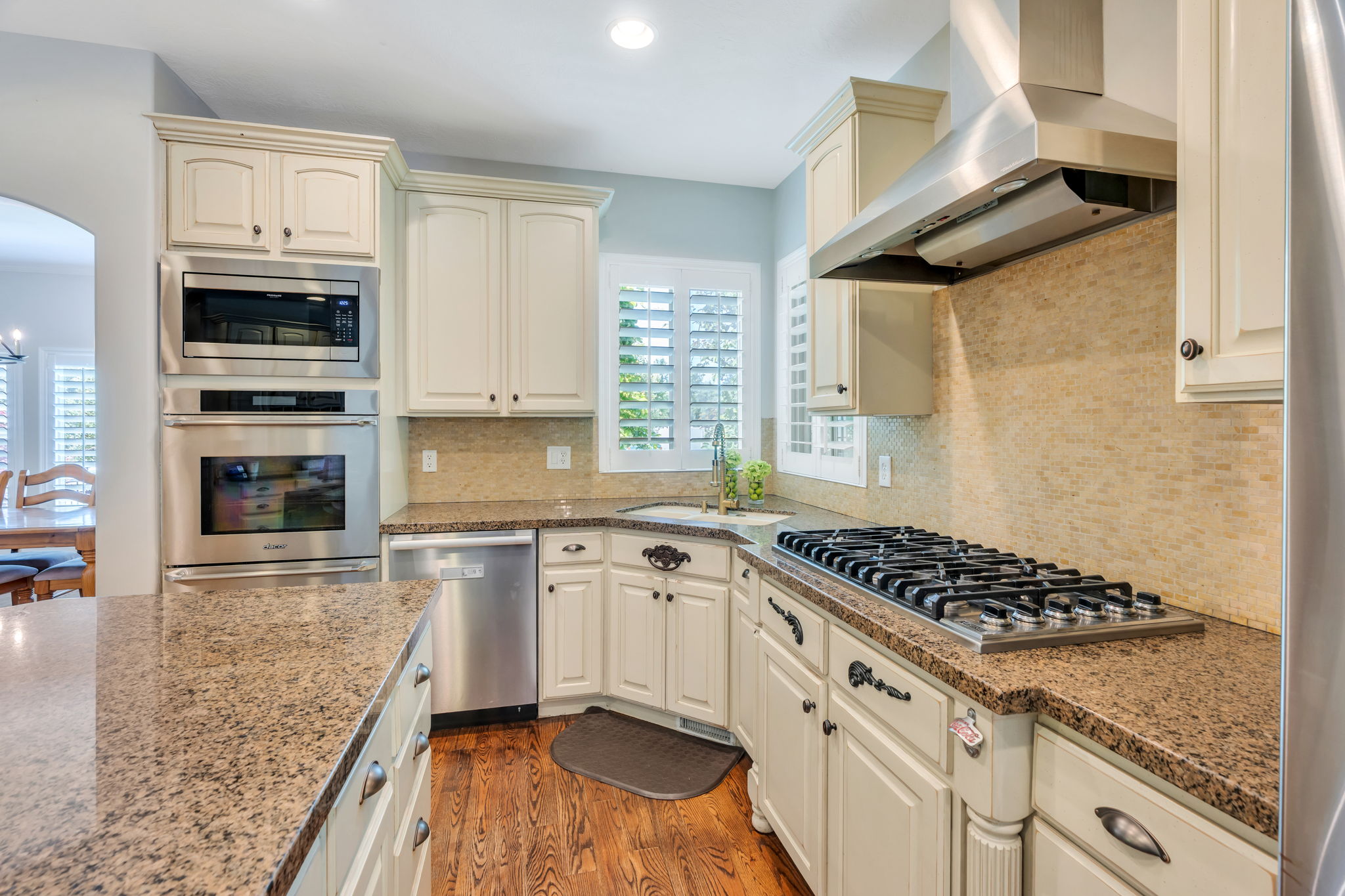 Gourmet kitchen featuring granite countertops, a built-in stainless steel oven and microwave, a gas cooktop with a stainless steel range hood, and custom cabinetry