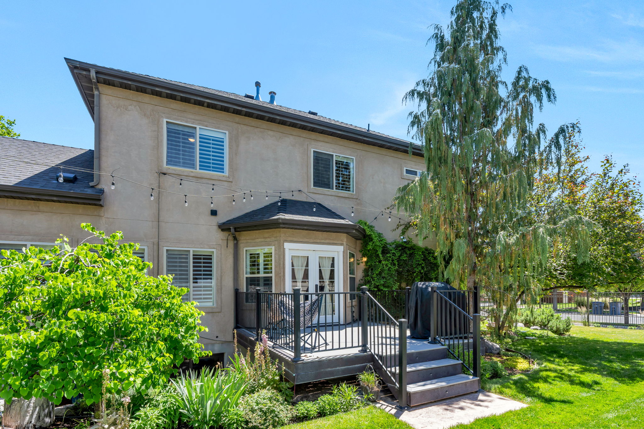 Rear exterior featuring a multi-level deck with black railings, stucco siding, and a dark shingle roof