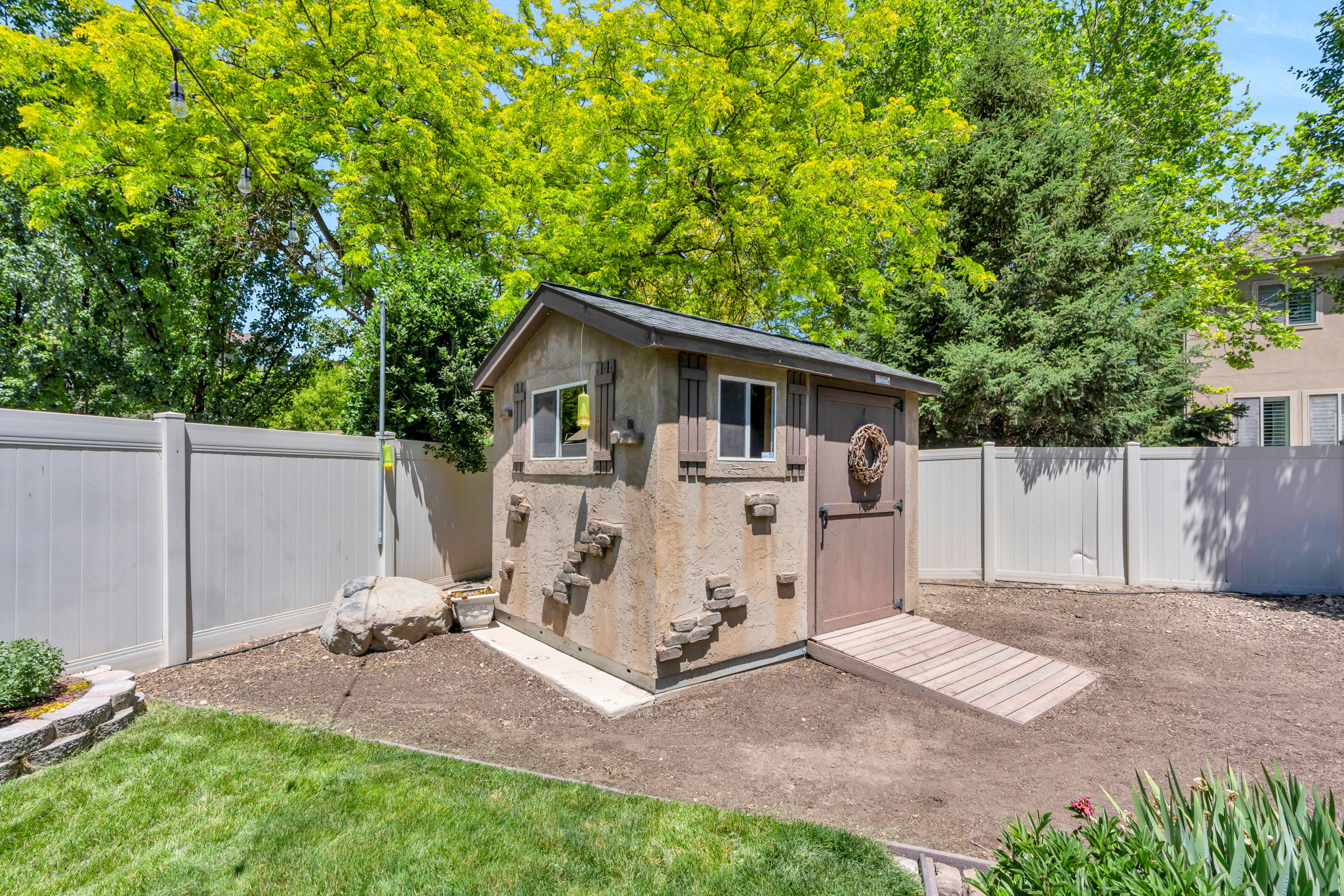 Detached storage shed with a gabled roof and textured exterior, featuring a wood door, two windows with shutters, and a wood ramp