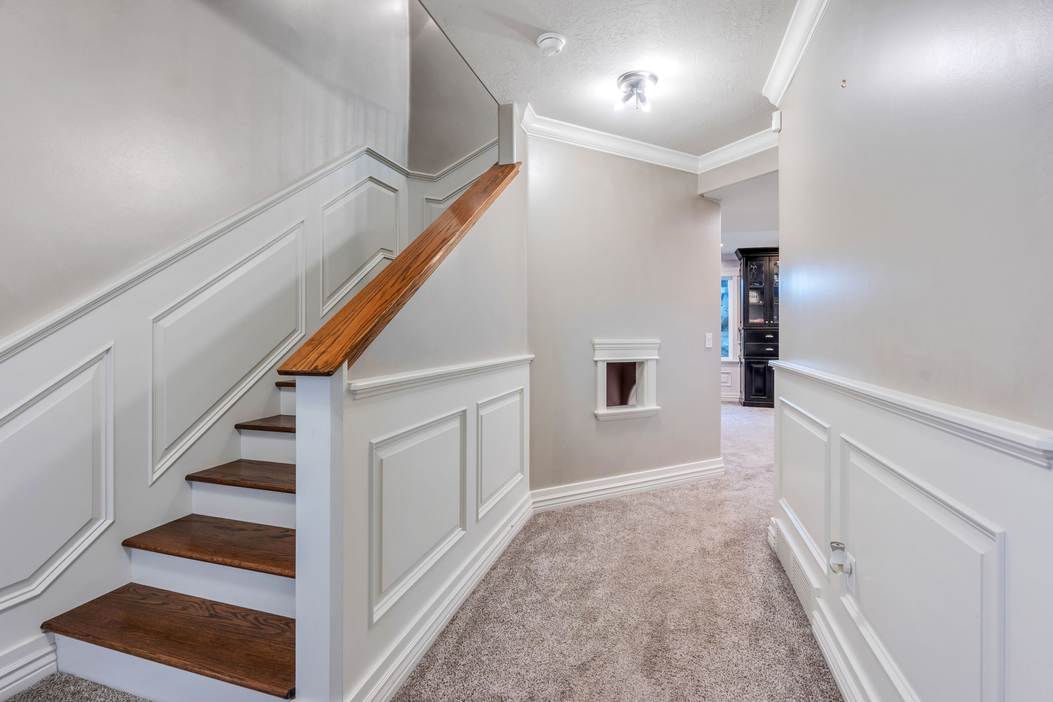 Staircase and hallway featuring wainscoting, a wood-finish handrail, wood-finish stair treads, and carpeted flooring