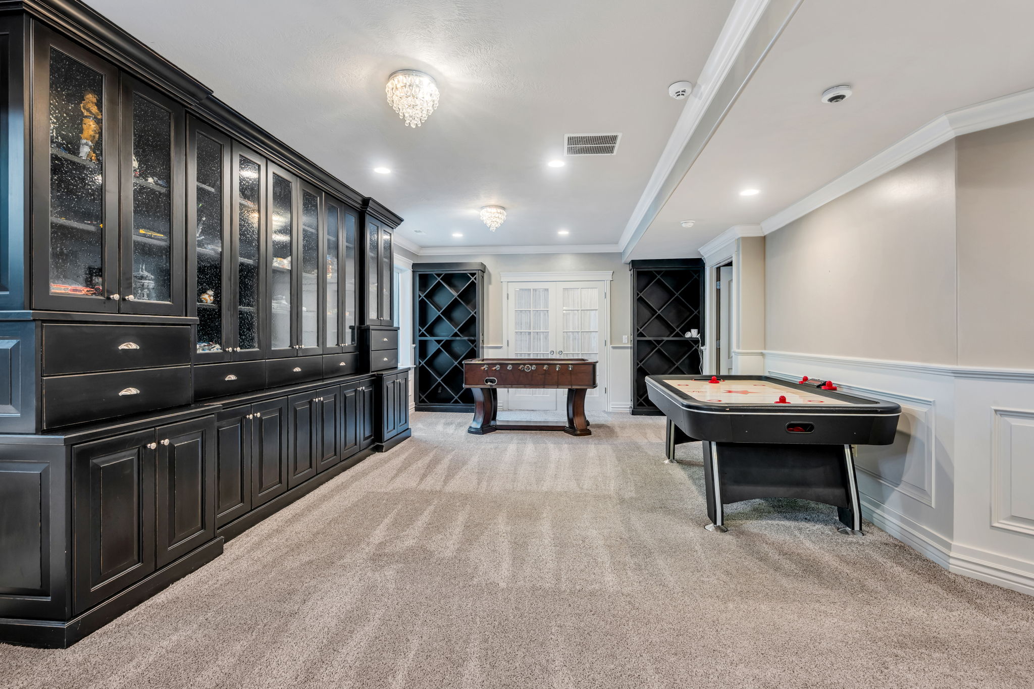 Extensive built-in black cabinetry with glass-front uppers and silver hardware, complemented by recessed lighting and two chandelier fixtures