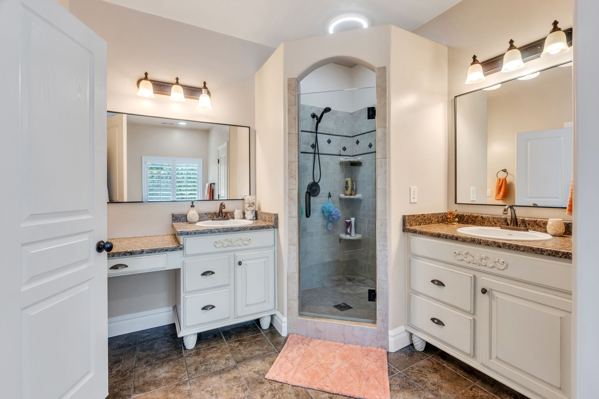 Bathroom featuring a tiled archway shower with glass enclosure, dual vanity sinks, and wood-finish flooring