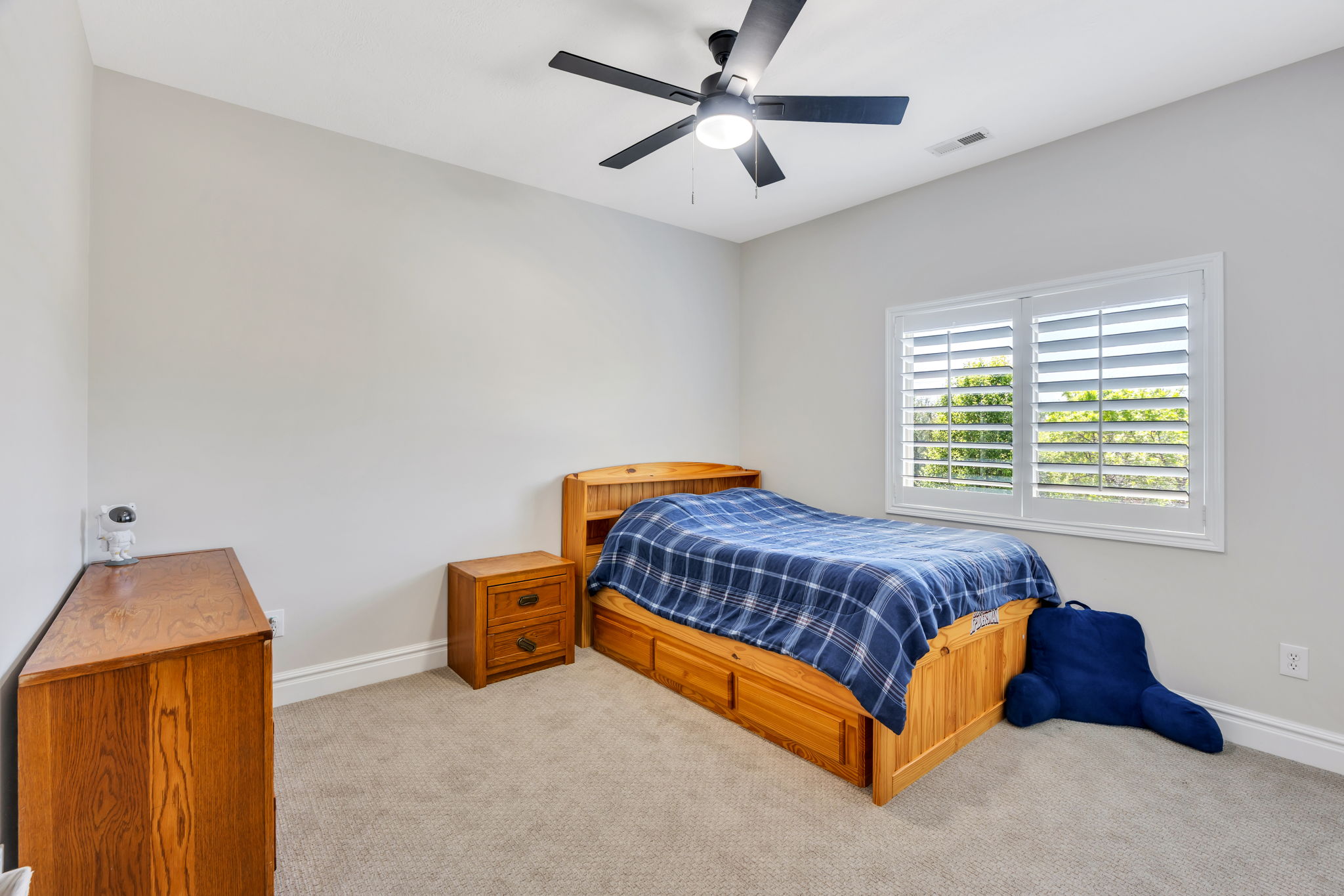 Bedroom featuring a ceiling fan with integrated lighting, a window with white plantation shutters, neutral carpeting, and white baseboards
