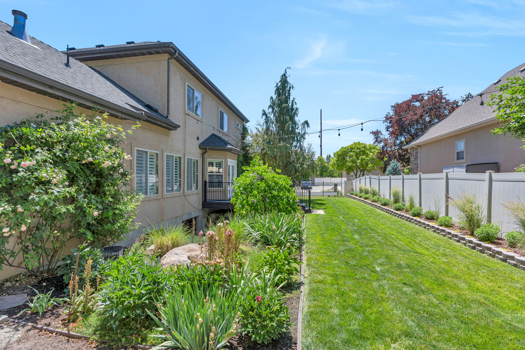 Spacious rear yard with a manicured lawn, established landscaping, and a white vinyl privacy fence