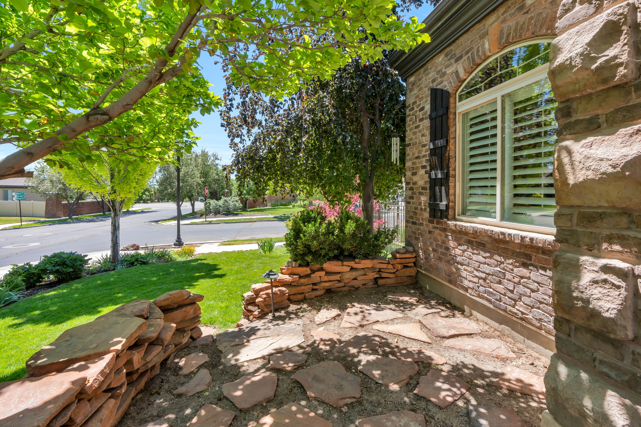 Stone and brick exterior featuring an arched window with white plantation shutters, a flagstone patio, and a manicured lawn