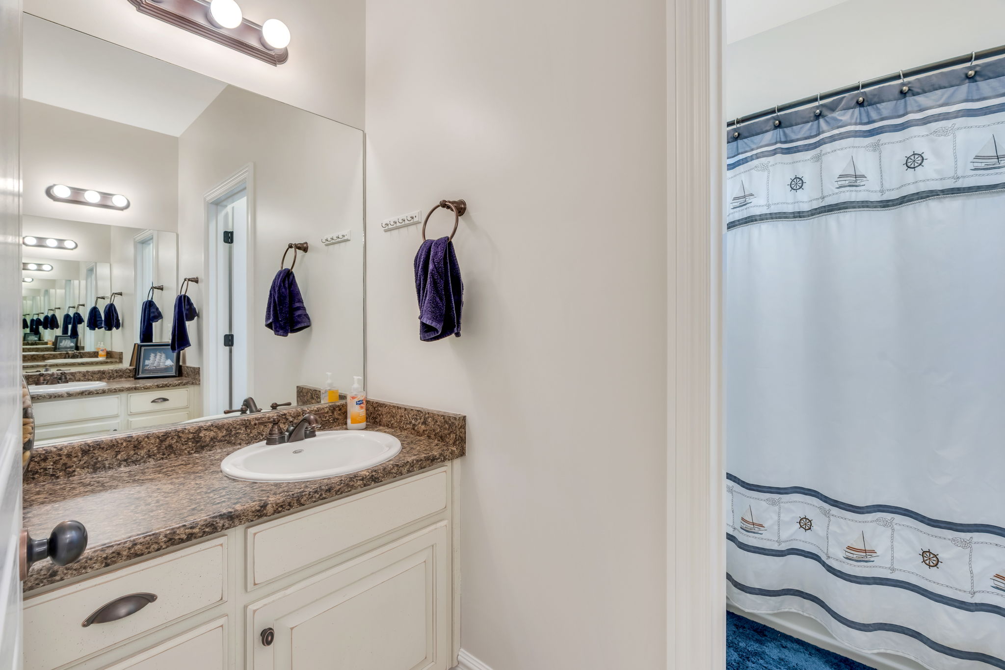 Bathroom vanity featuring a single basin, dark speckled countertop, and white cabinetry with dark hardware