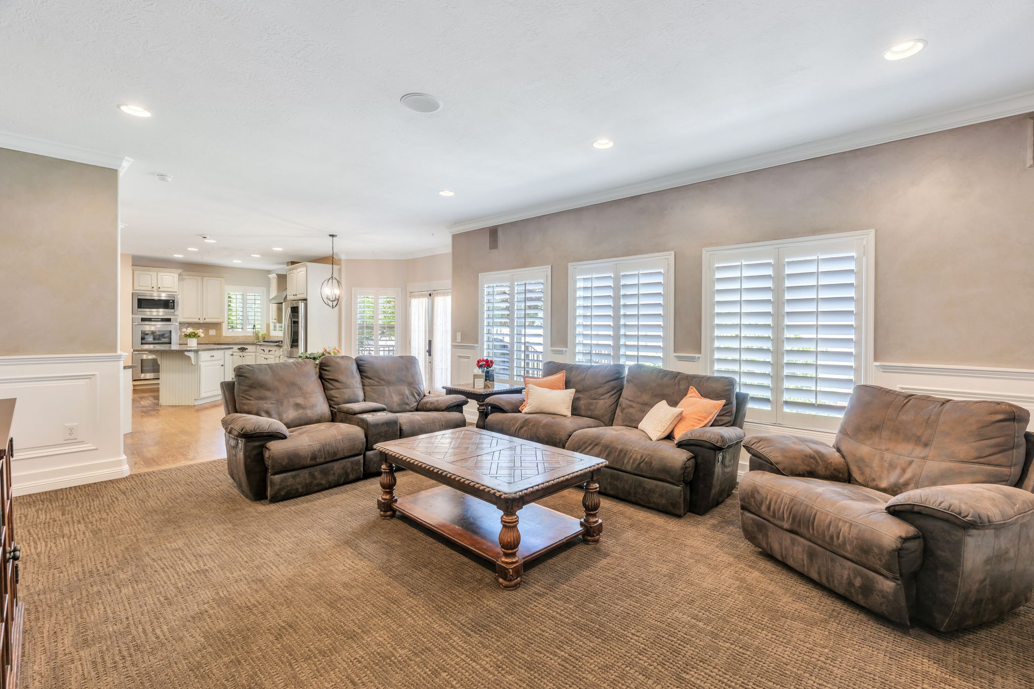 Spacious living area featuring neutral textured carpeting, recessed lighting, and white plantation shutters on multiple windows