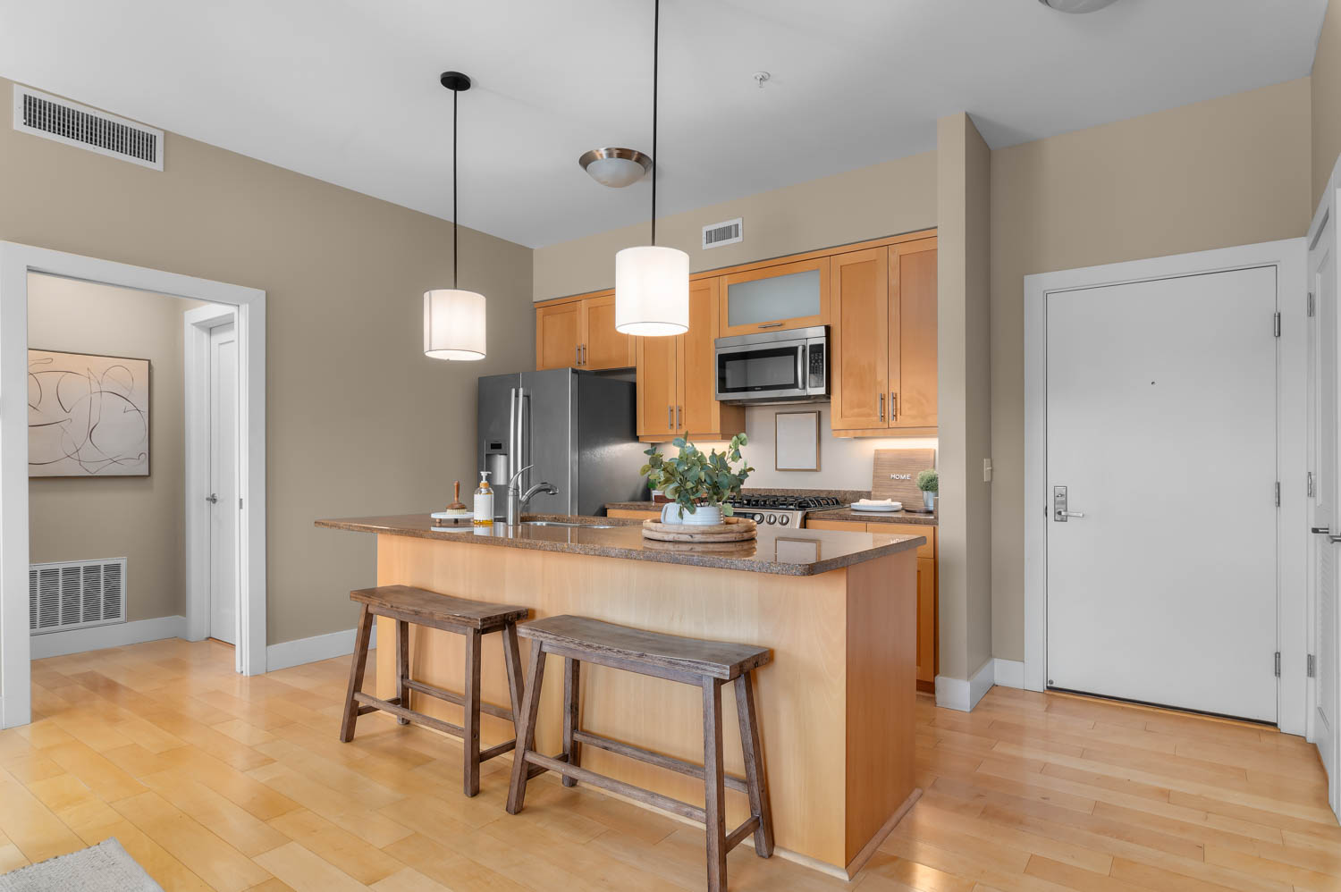 Kitchen featuring a granite-top island with pendant lighting, stainless steel appliances, wood-finish cabinetry, and light wood-finish flooring