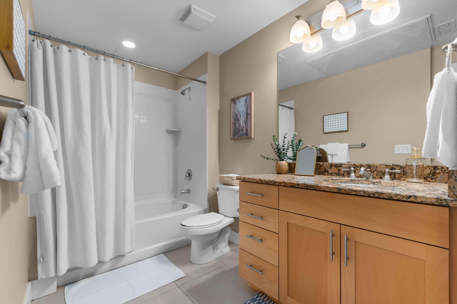 Bathroom featuring a light wood-finish vanity with ample storage, a granite-finish countertop, and a vanity mirror with a four-light fixture