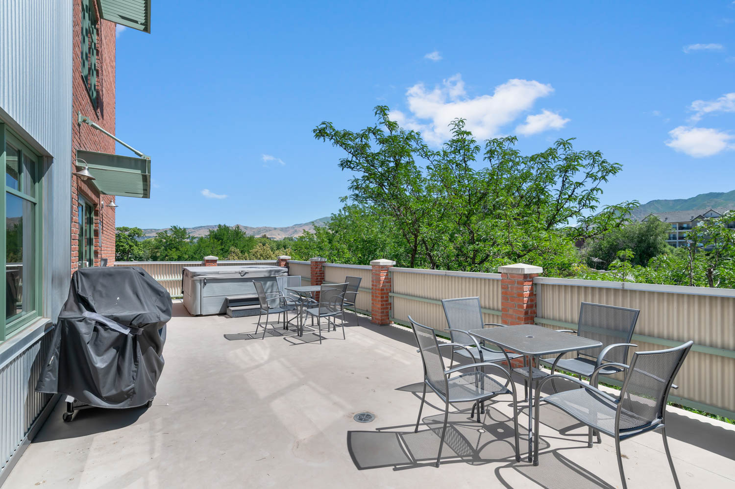 Expansive community concrete patio featuring a hot tub, brick columns, and a corrugated metal fence