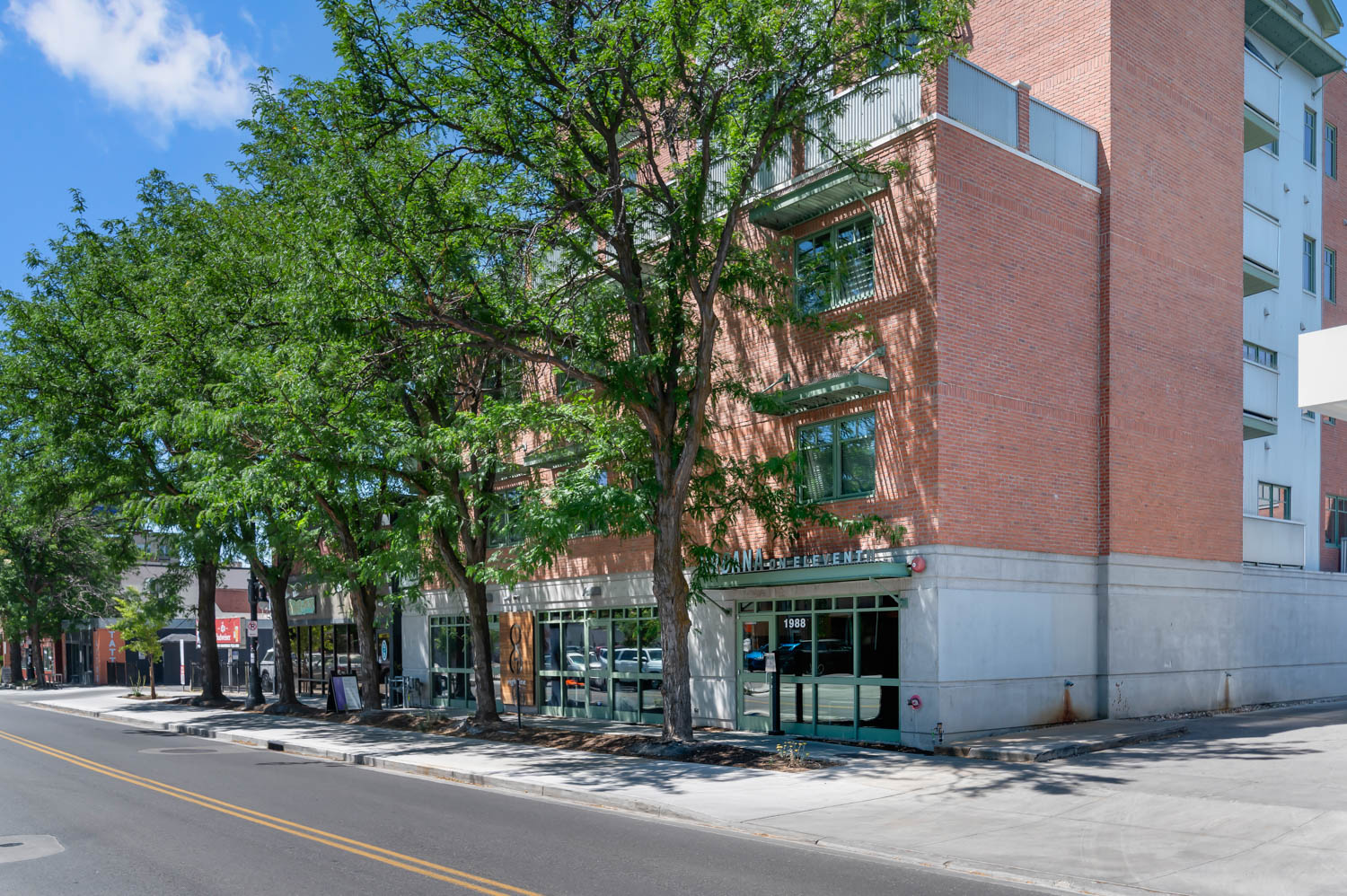 Brick facade building with multiple levels, featuring green window awnings and a ground-floor retail space with large glass windows