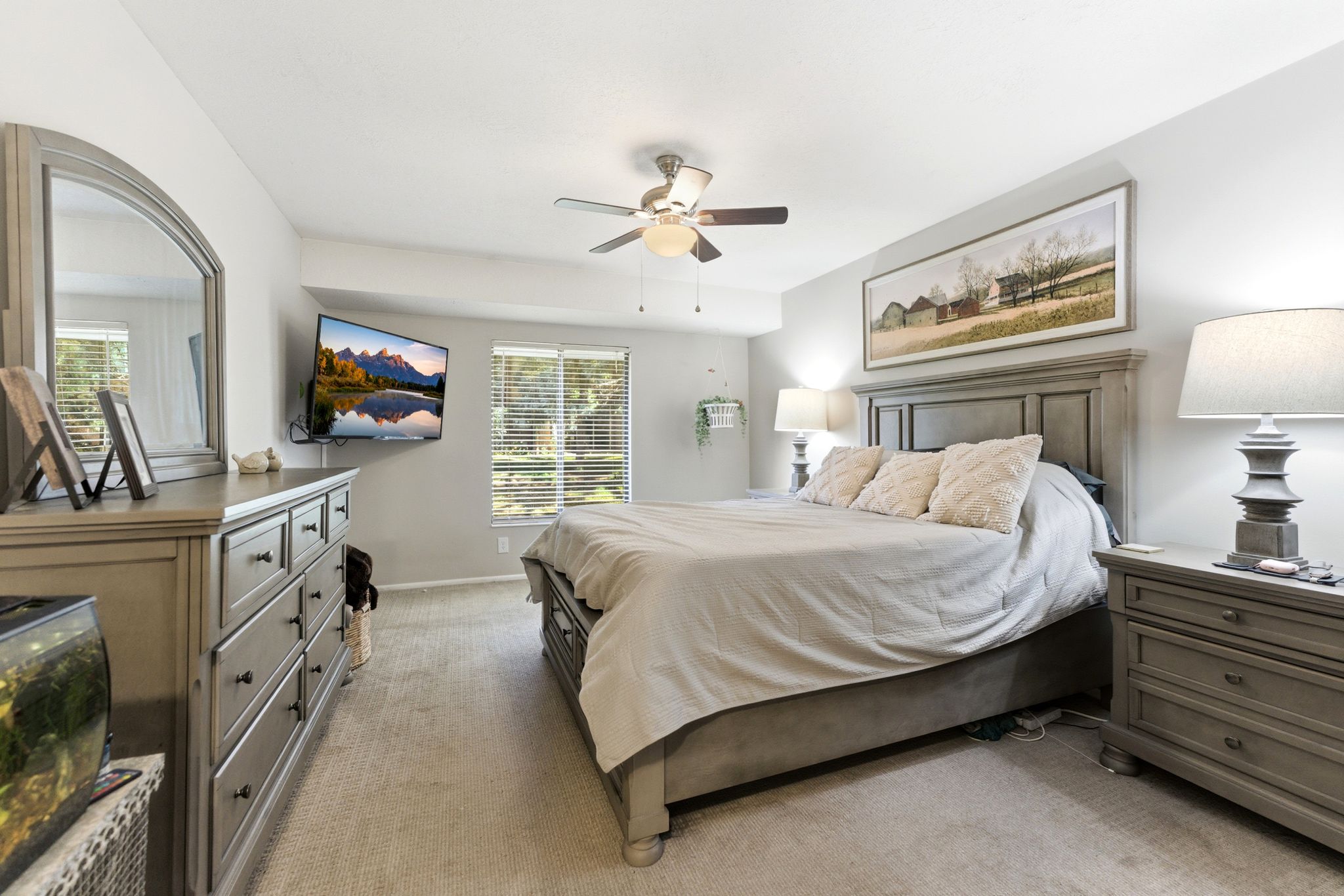 Spacious bedroom featuring light-toned carpeting, multiple large windows with blinds, and a ceiling fan with integrated lighting