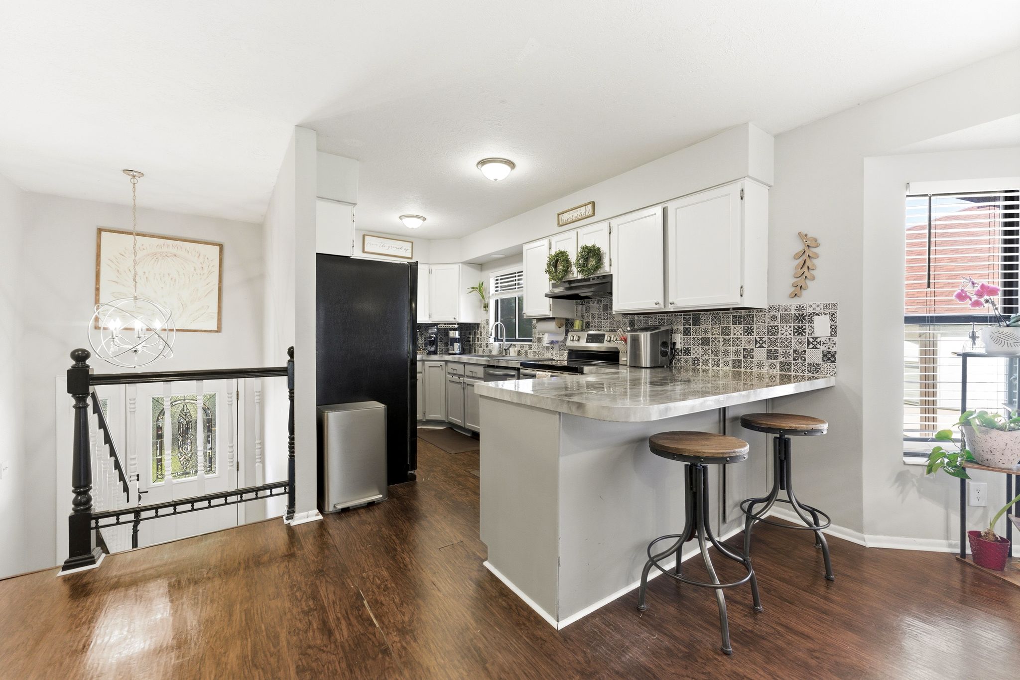 Open-concept kitchen featuring wood-finish flooring, white cabinetry, a patterned tile backsplash, and a breakfast bar with a solid surface countertop
