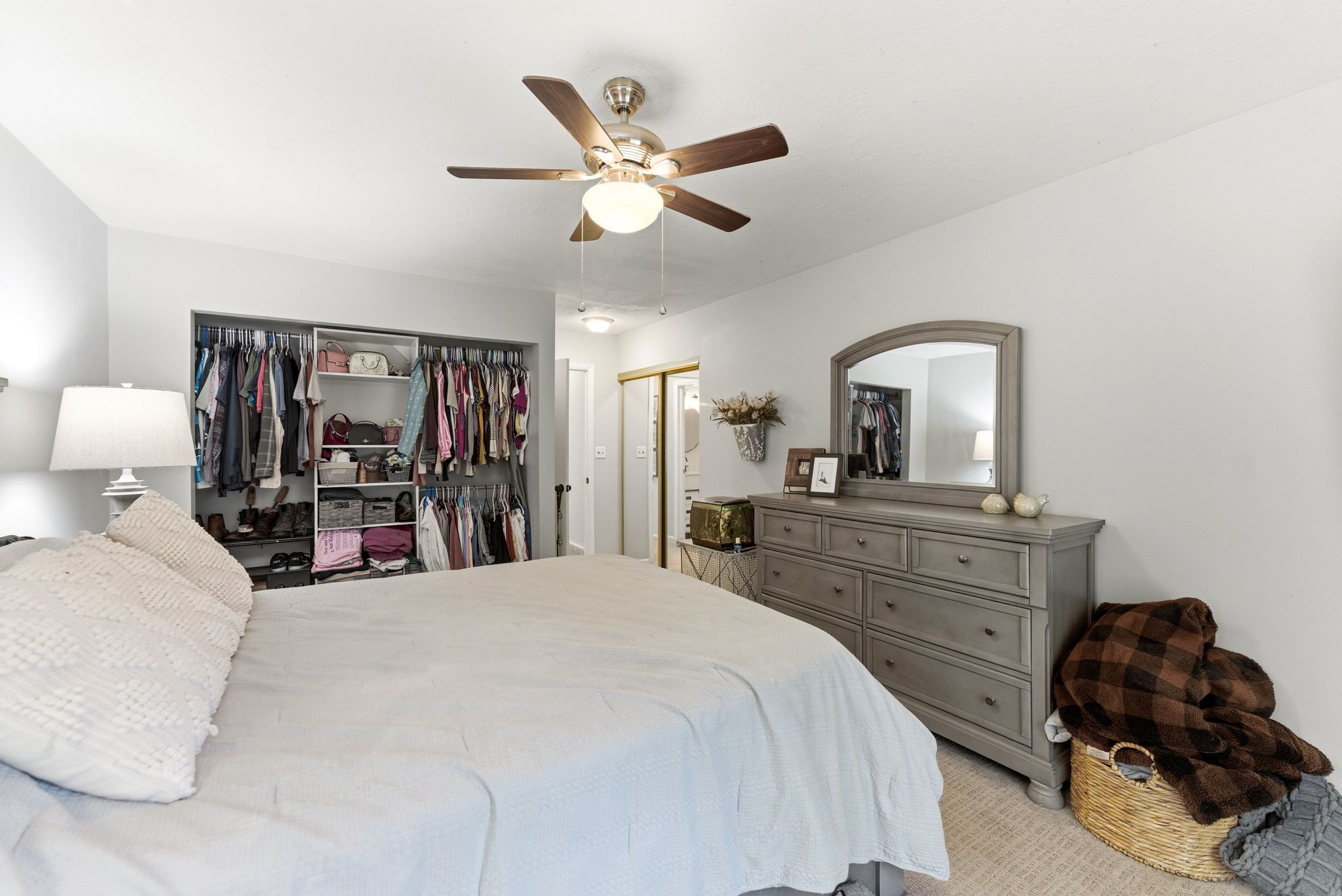 Bedroom featuring a ceiling fan with integrated lighting, recessed closet with built-in shelving, two white doors, and light-colored carpeting