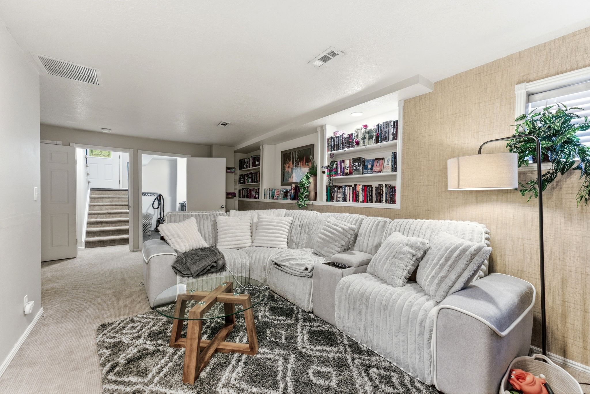 Open living area with built-in shelving, textured wall covering, and neutral carpet flooring