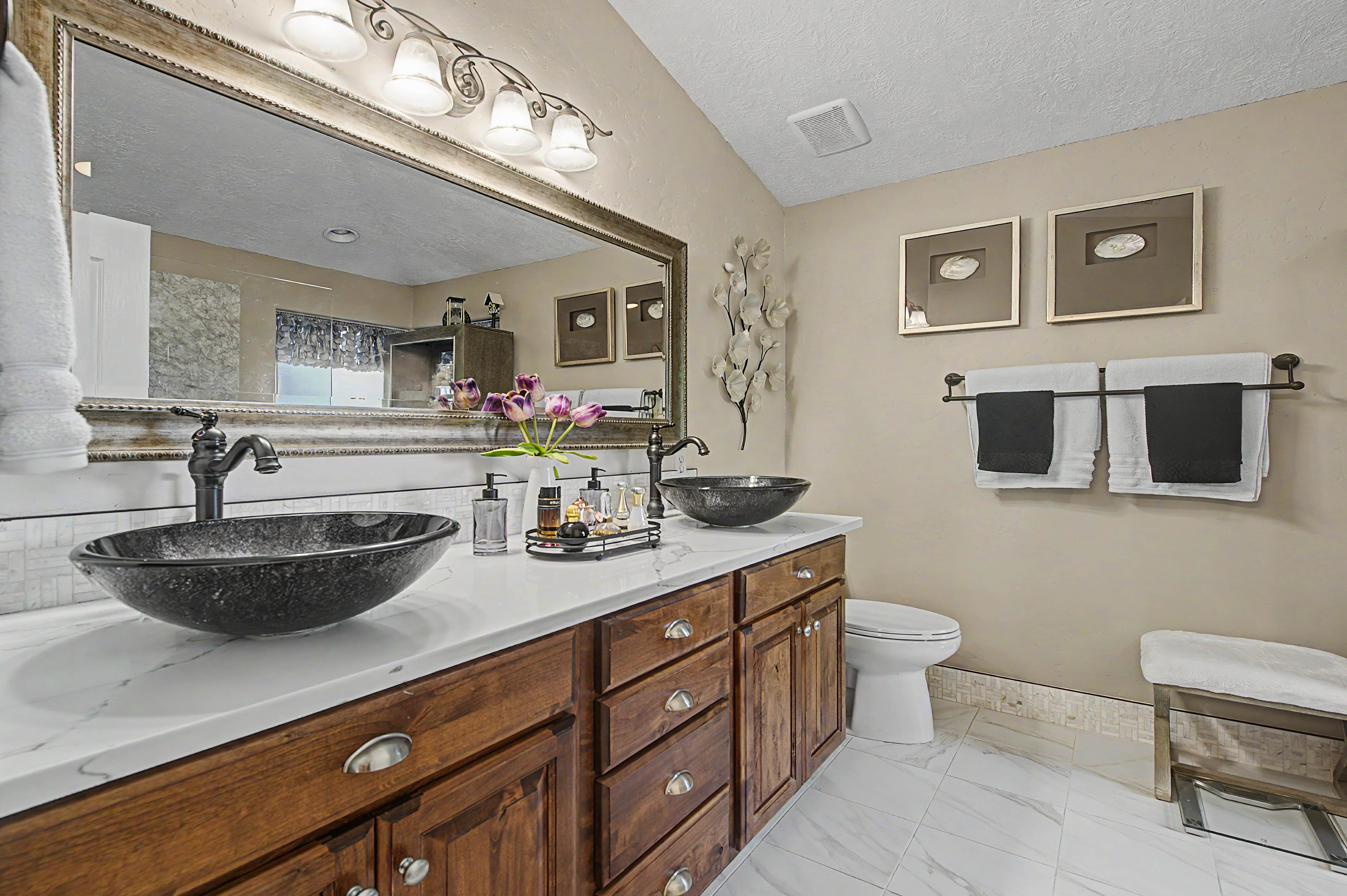 Dual vessel sinks with bronze-finish fixtures set on a white countertop, complemented by a wood-finish vanity with ample storage