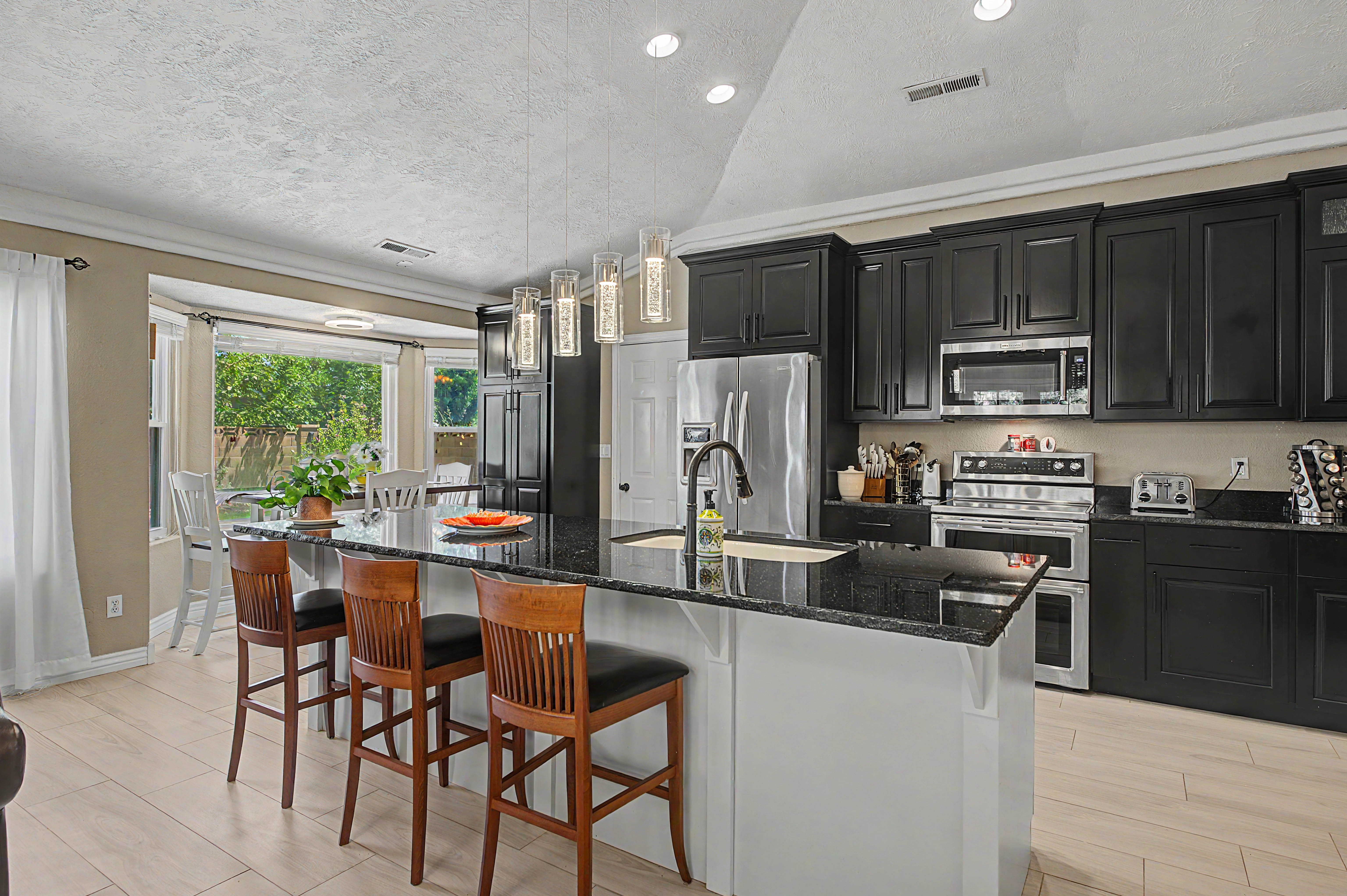 Spacious kitchen featuring an expansive center island with seating, dark cabinetry, stainless steel appliances, and light wood-finish flooring