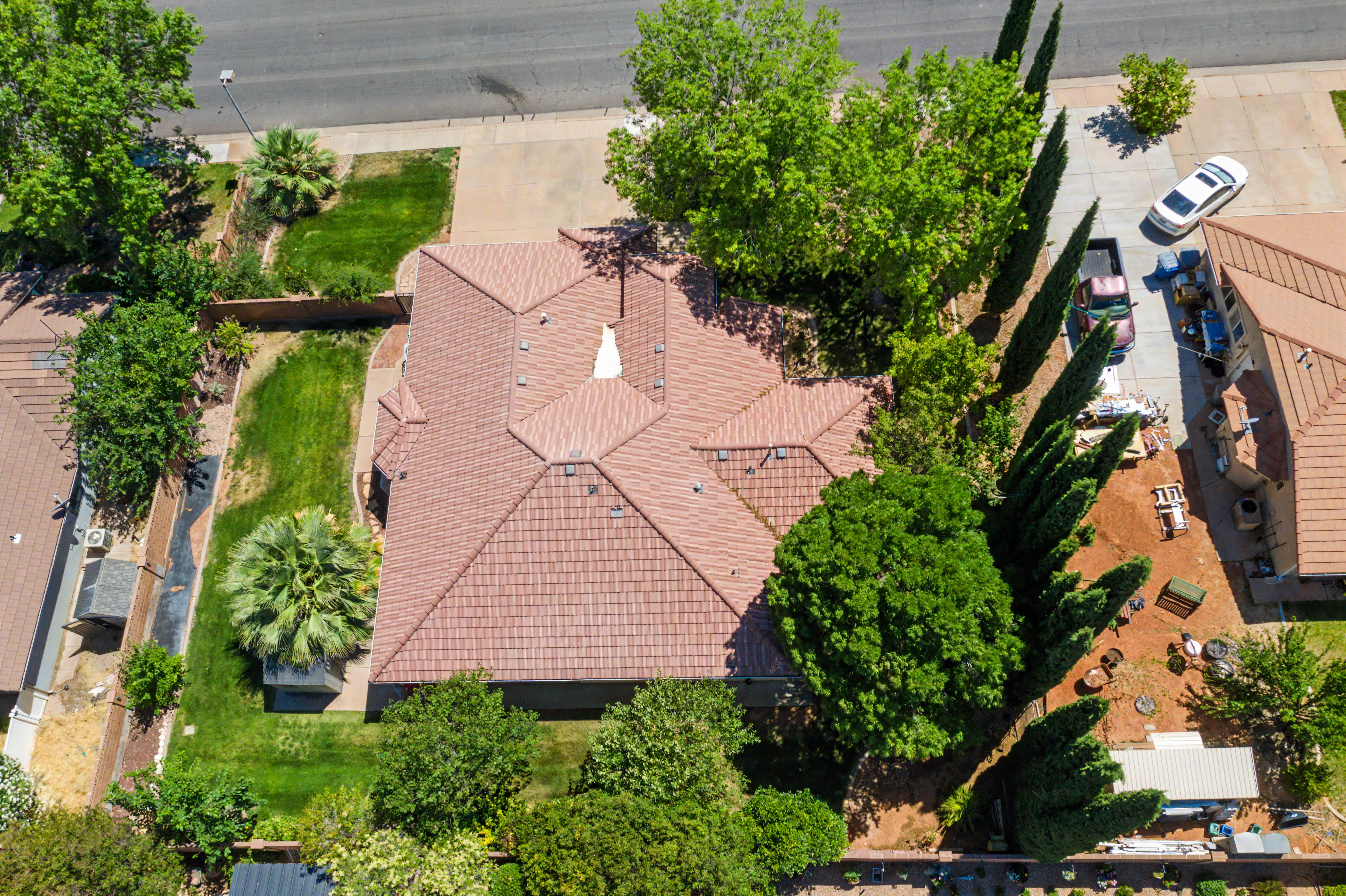 Property featuring a terracotta tile roof, a verdant lawn, mature trees, a paved driveway, and a perimeter fence