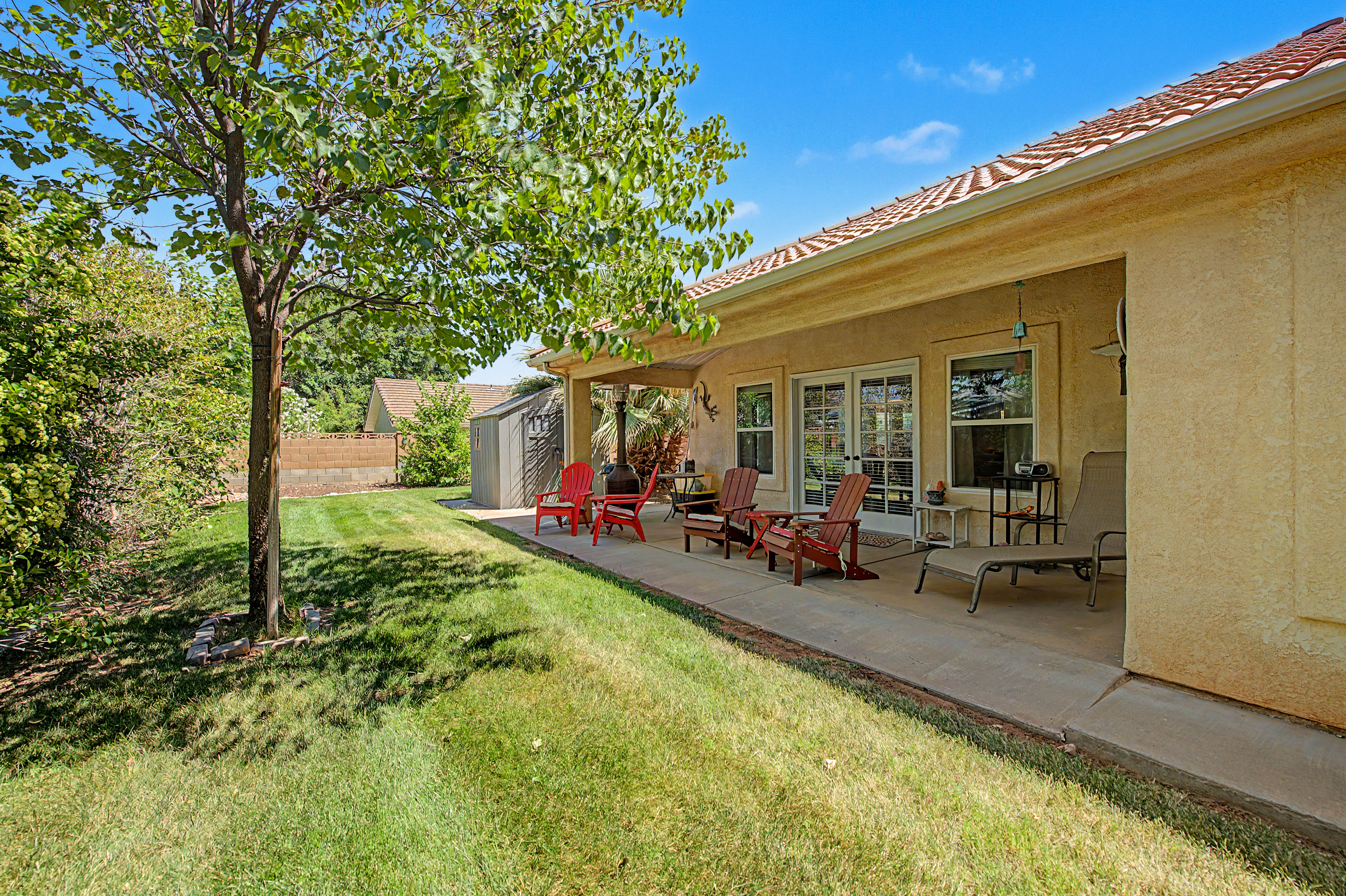 Expansive backyard featuring a manicured lawn, established tree, and concrete patio