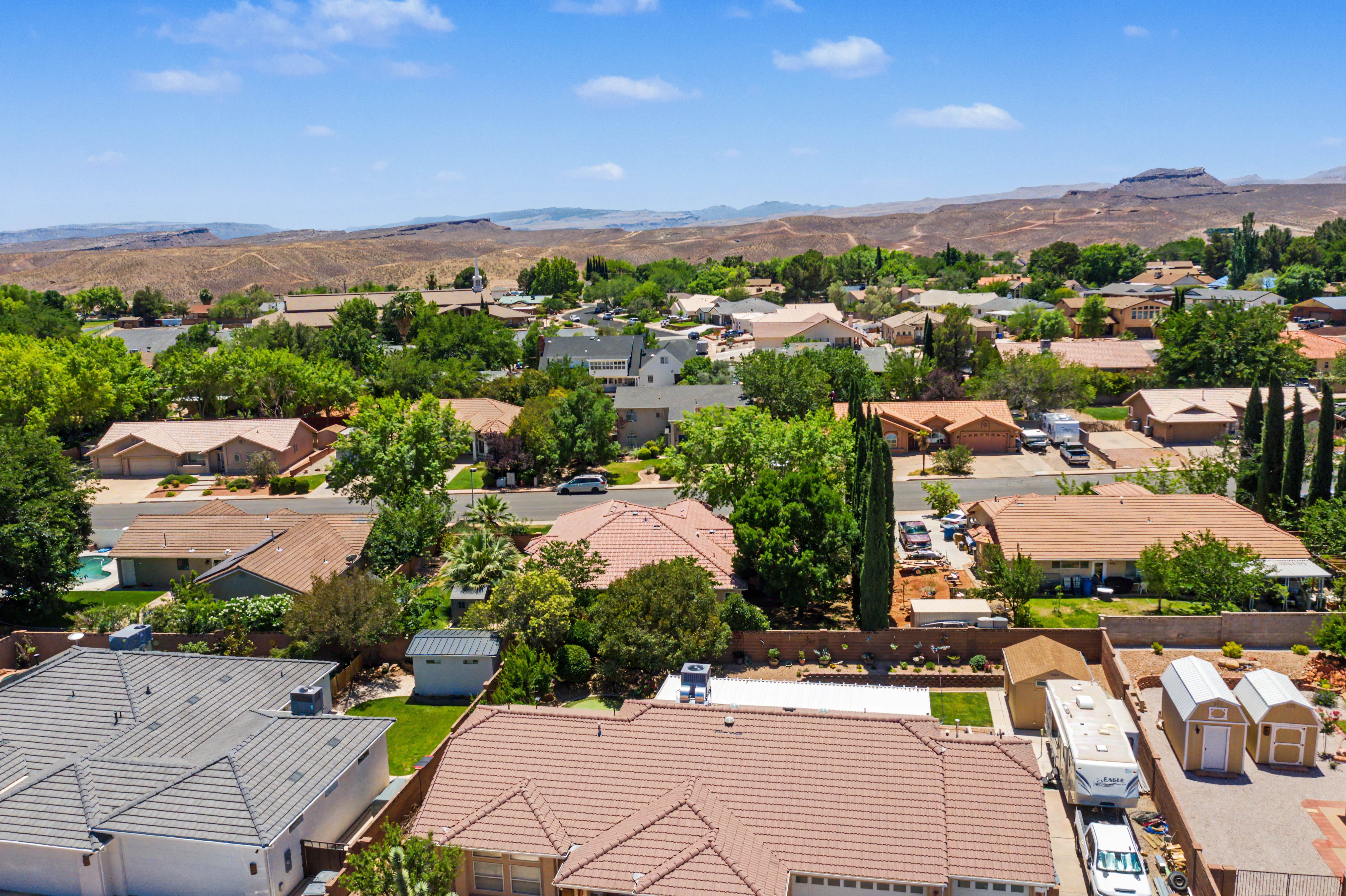 Aerial perspective showcasing a residential neighborhood with diverse roofing styles, mature trees, and distant natural landscapes