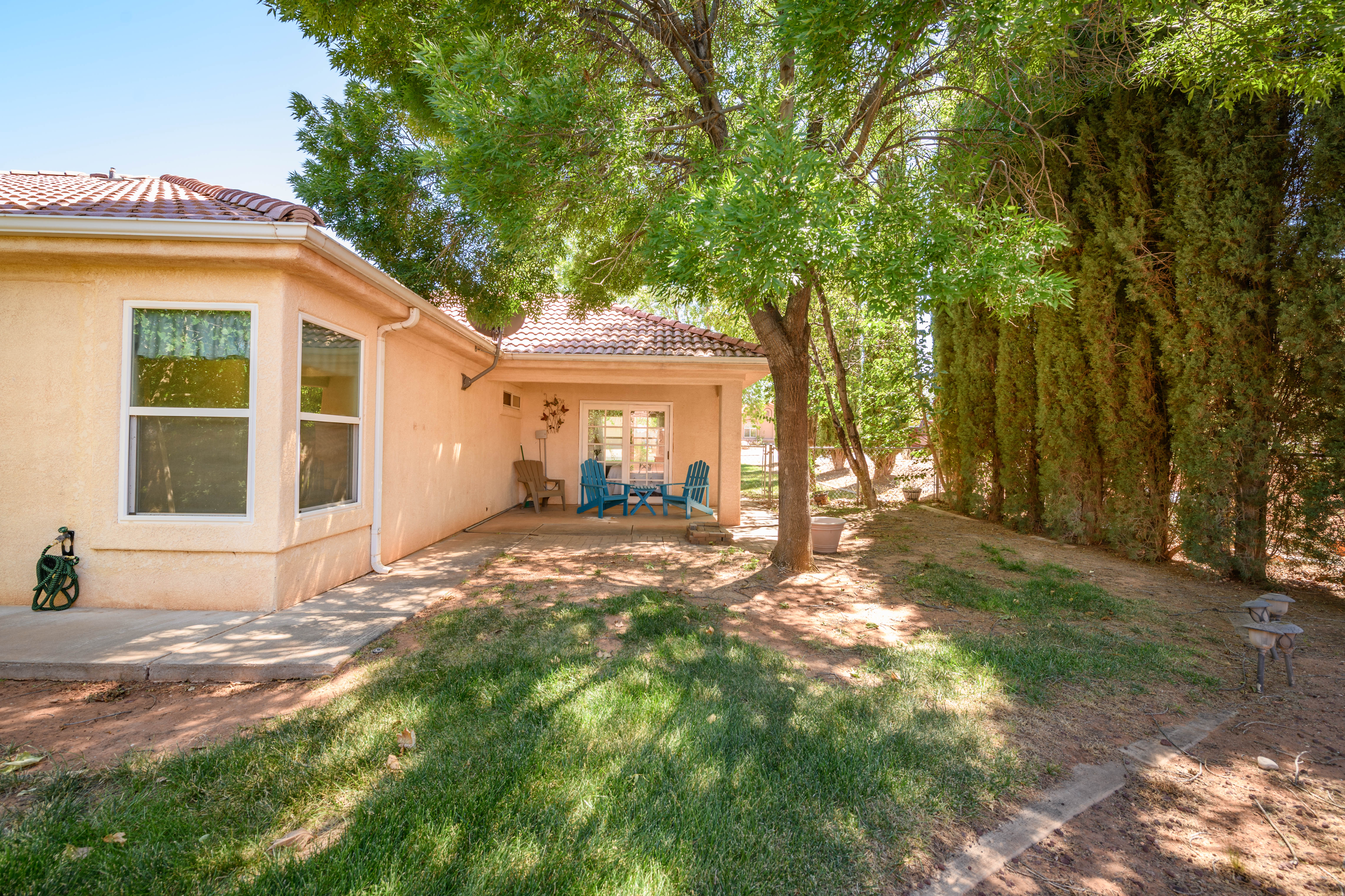 Backyard patio with a covered section, bordered by tall privacy trees